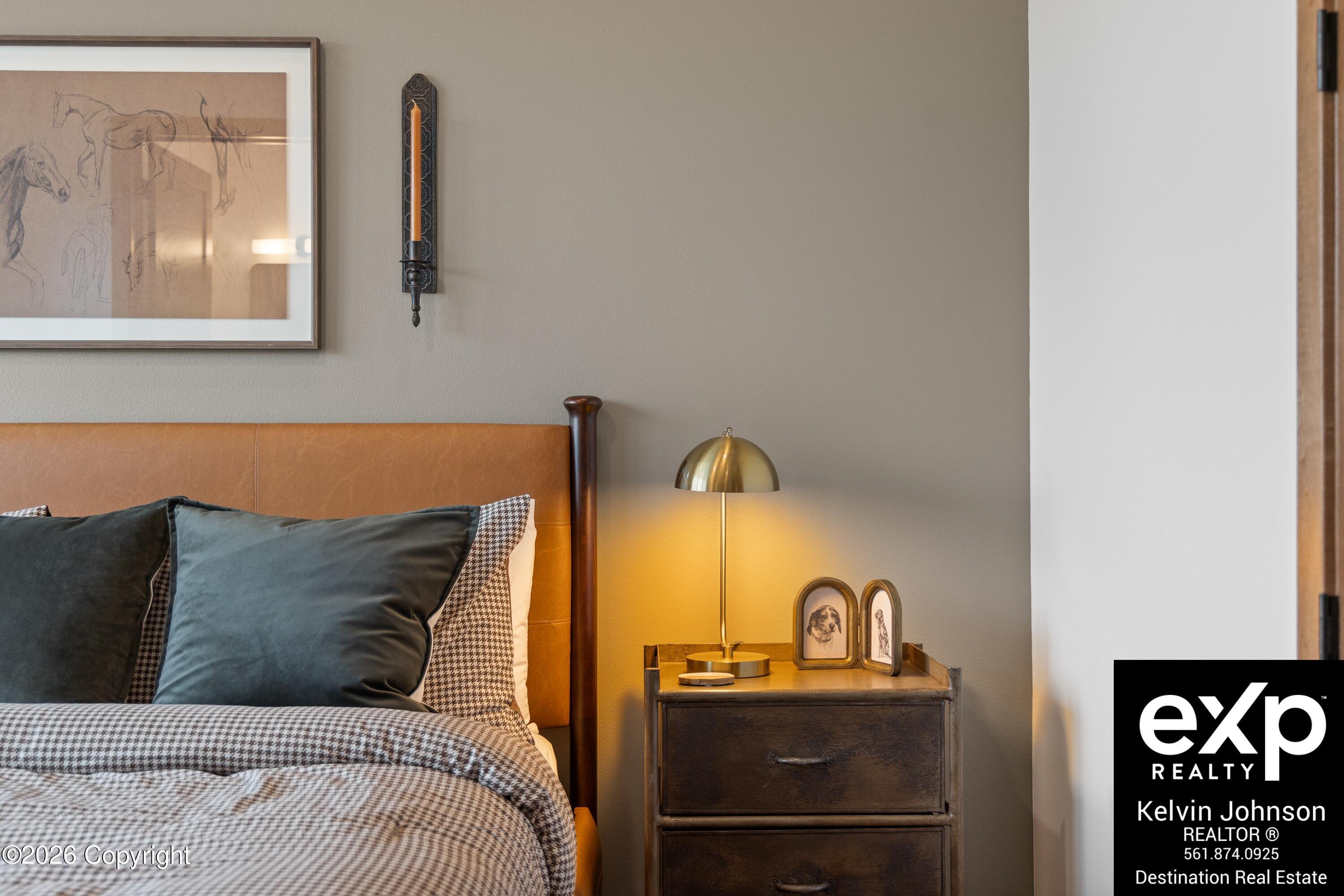 Furnished bedroom with a tan leather headboard, patterned bedding, and brass lamp beside a dark wooden nightstand.