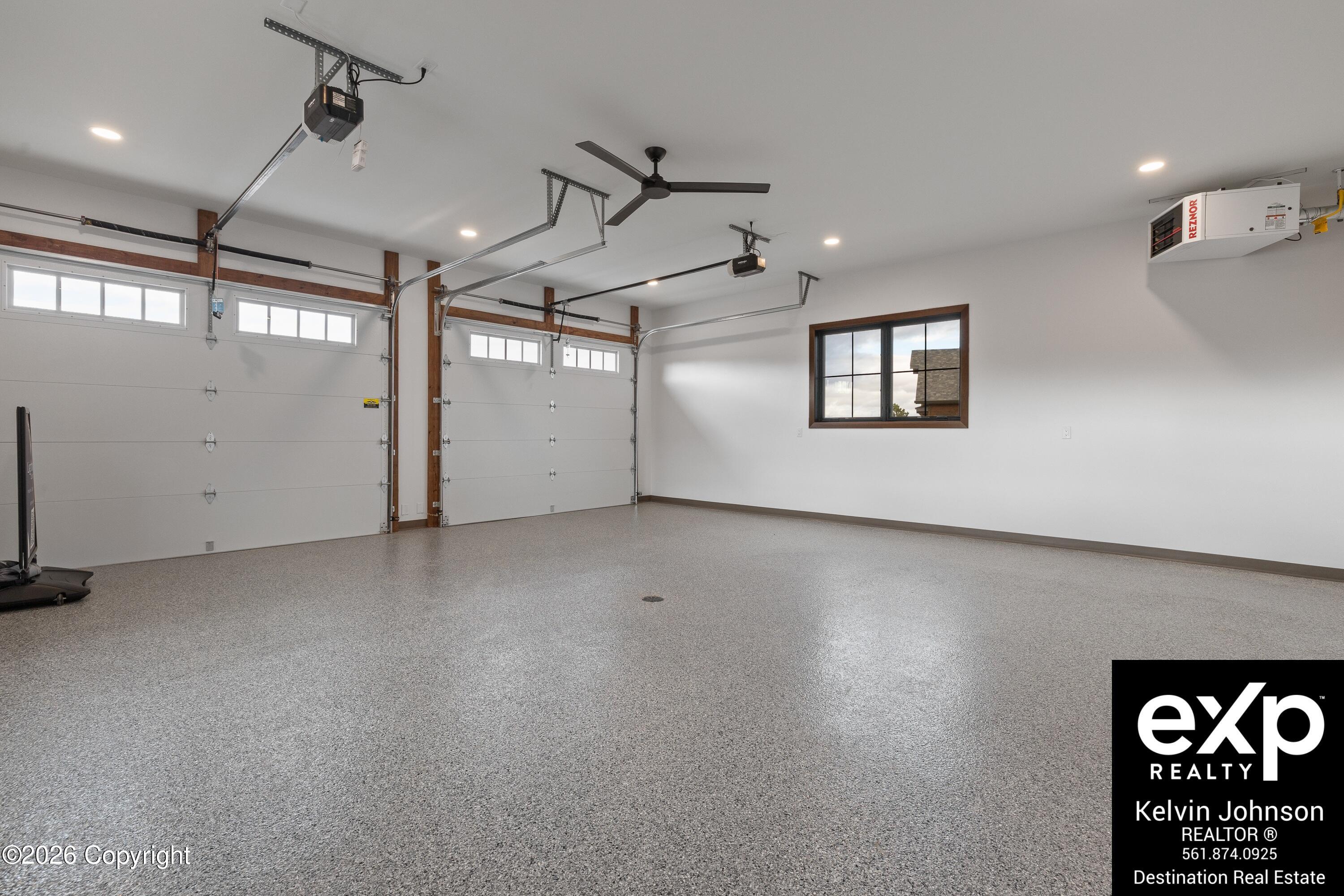 Three-car garage with a speckled floor, three overhead doors, and a ceiling fan.