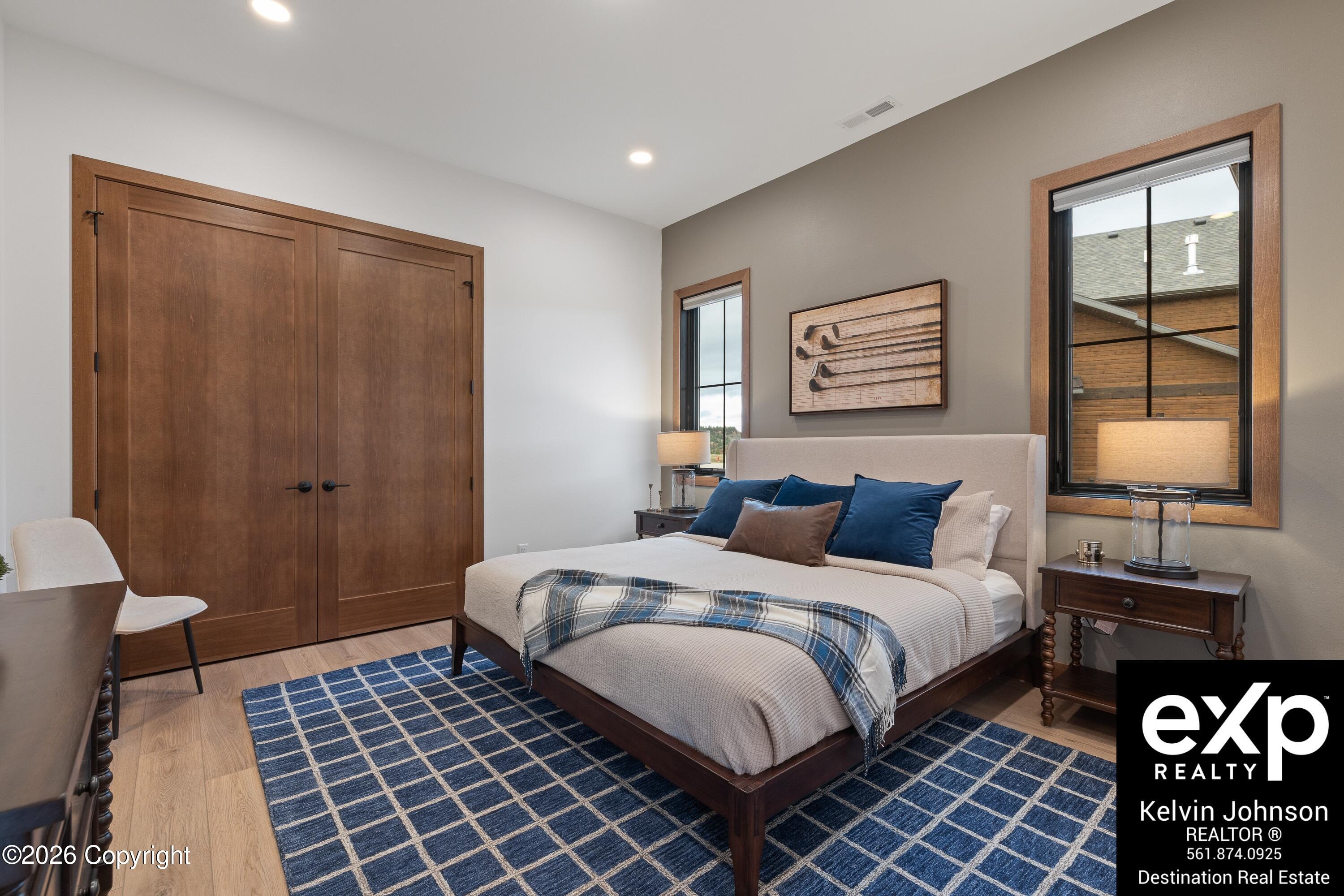 Staged bedroom with a white bed, blue pillows, wood double doors, and a blue grid rug.