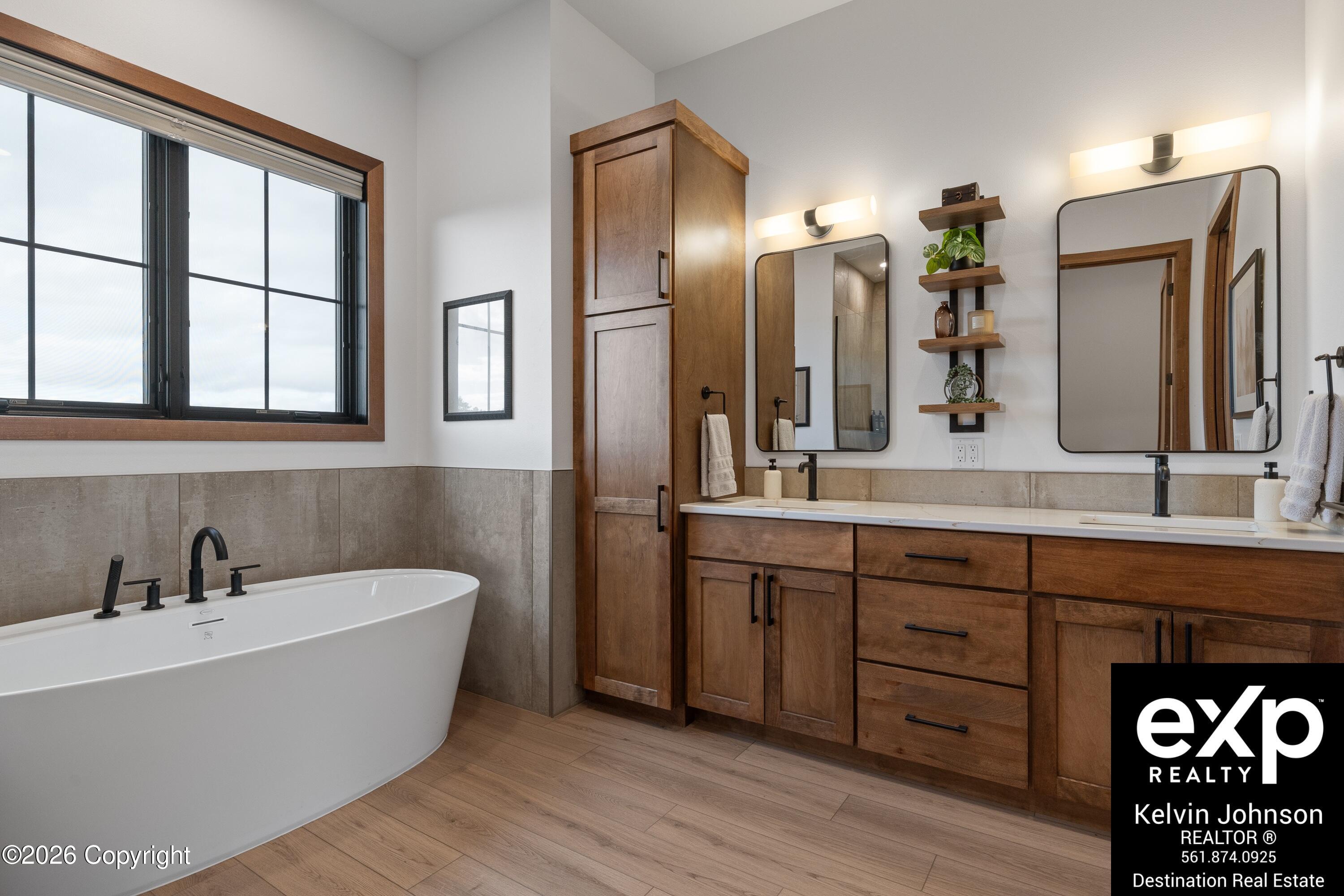 Bathroom with a freestanding soaking tub and long double vanity with warm wood cabinetry.