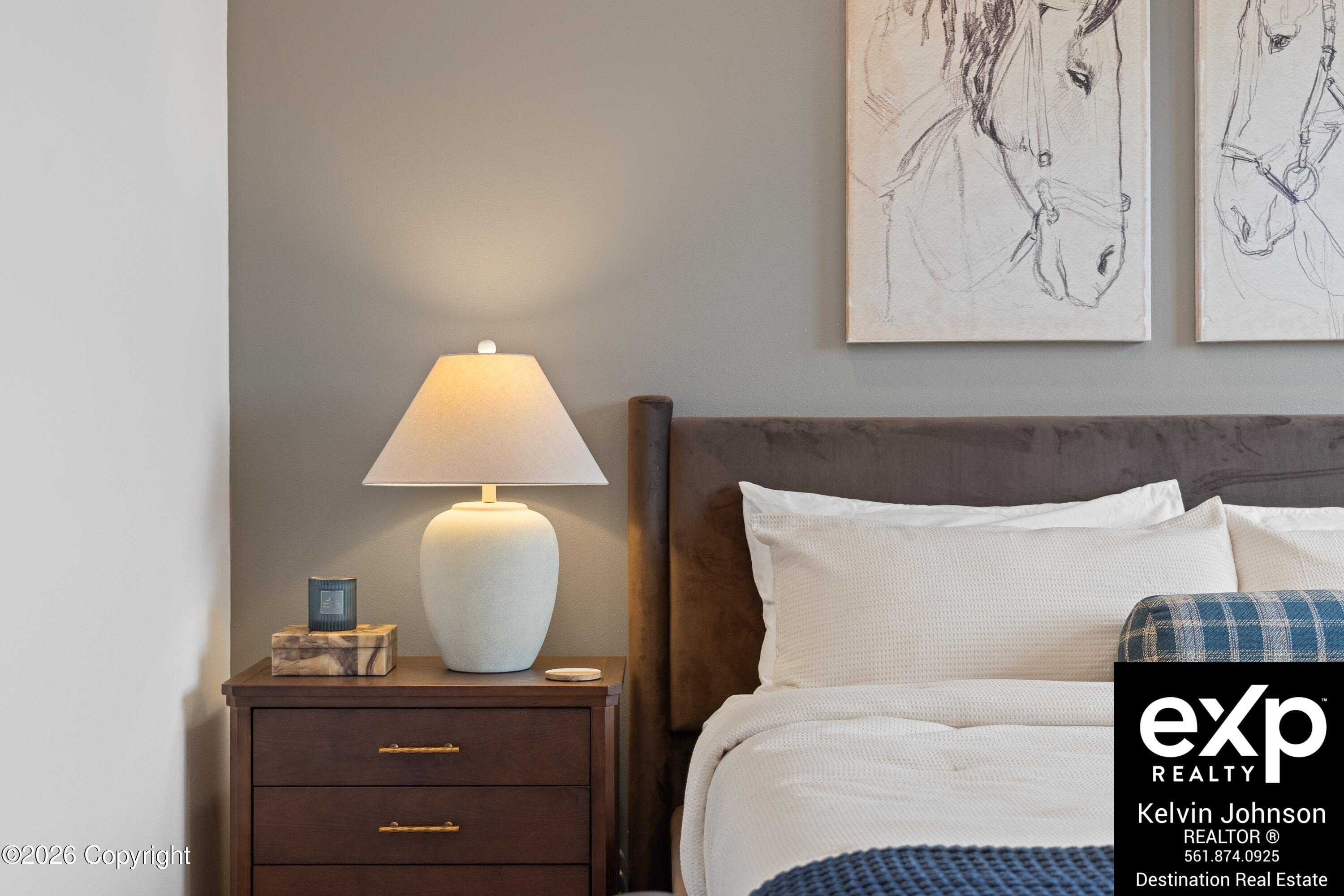 Staged bedroom with white bedding, a dark upholstered headboard, and horse sketches above the bed.