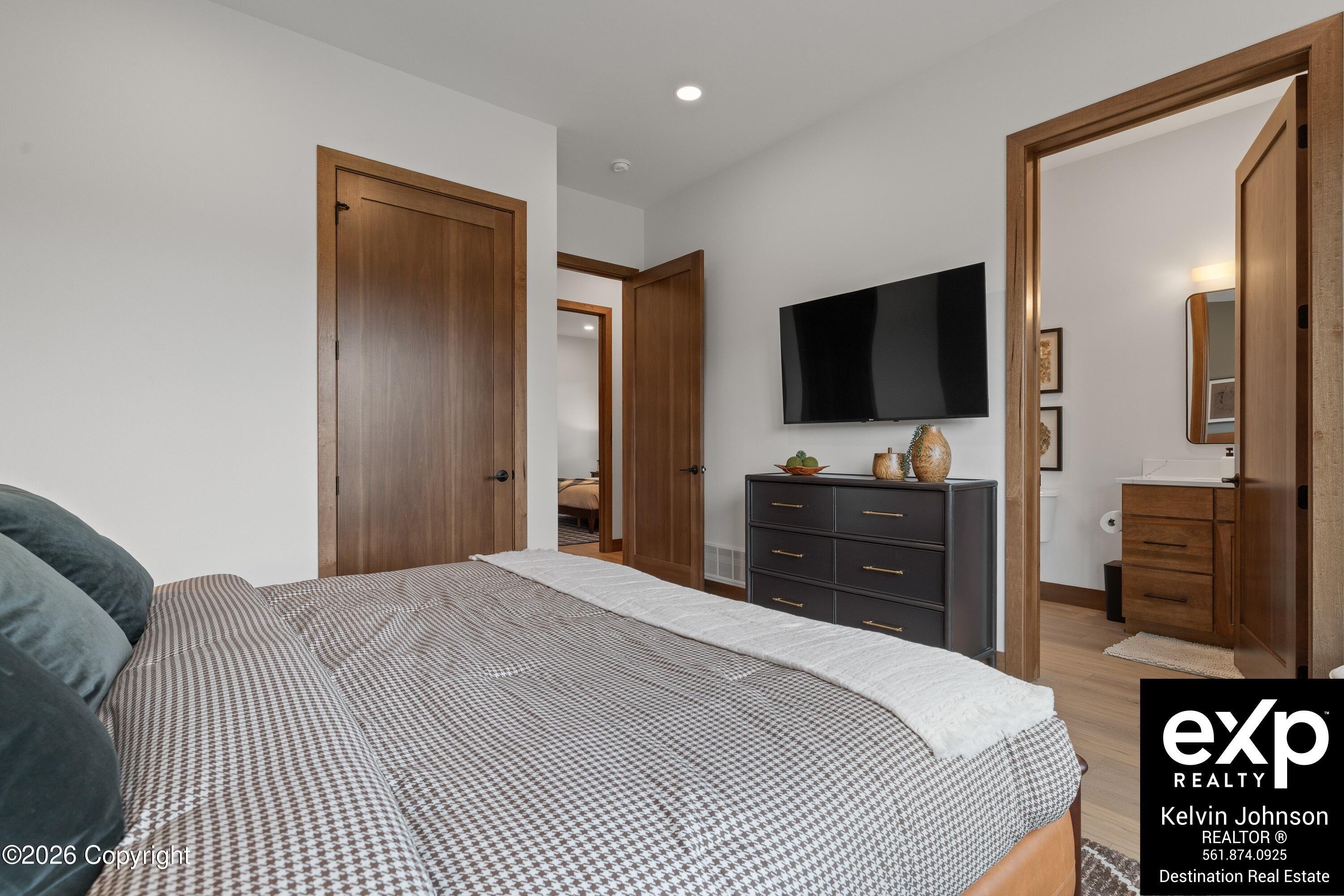 Furnished bedroom with a patterned bed, wall-mounted TV, and open doorway to the bathroom.