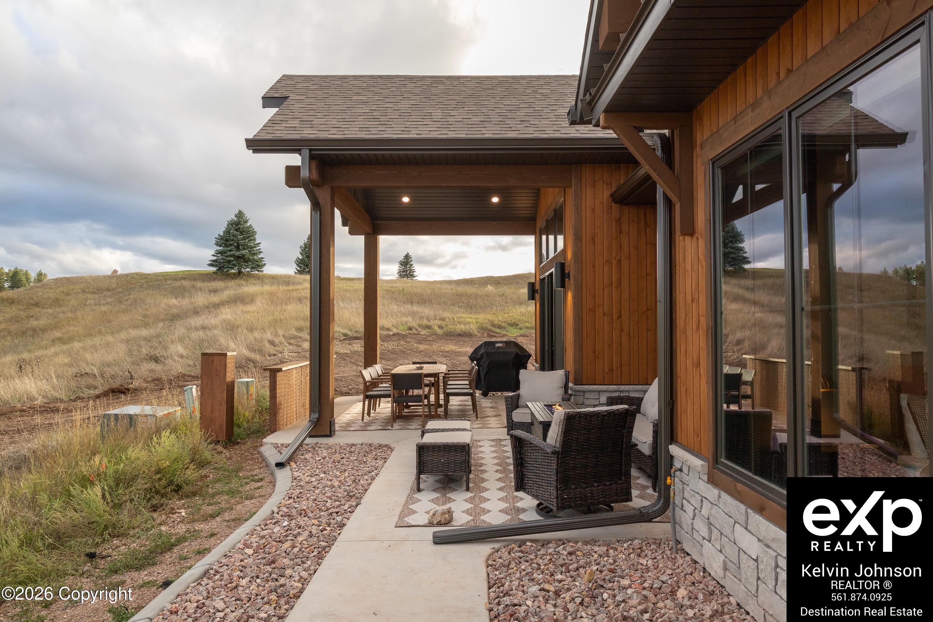 Covered patio with wicker seating, a dining area, and a grill overlooking grassy hills.