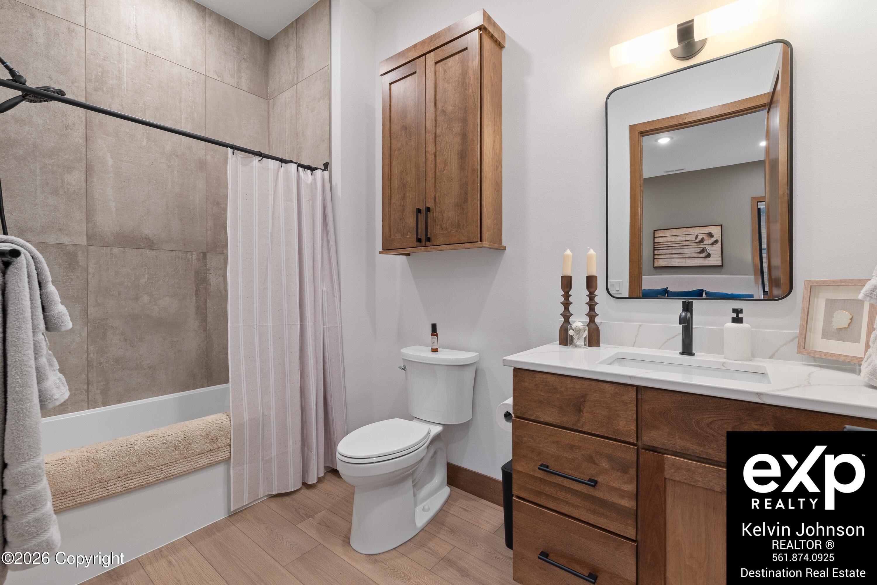 Bathroom with a wood vanity, large mirror, and tiled tub and shower.