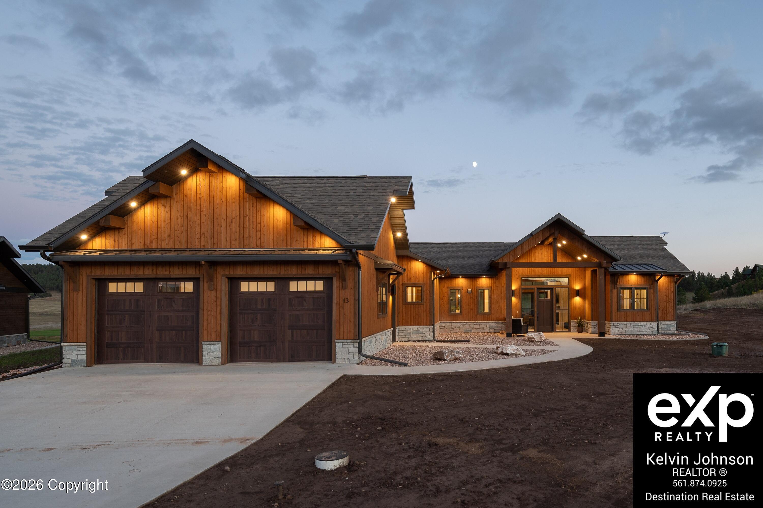 Wood-sided home with stone accents and two garage doors, illuminated at dusk.