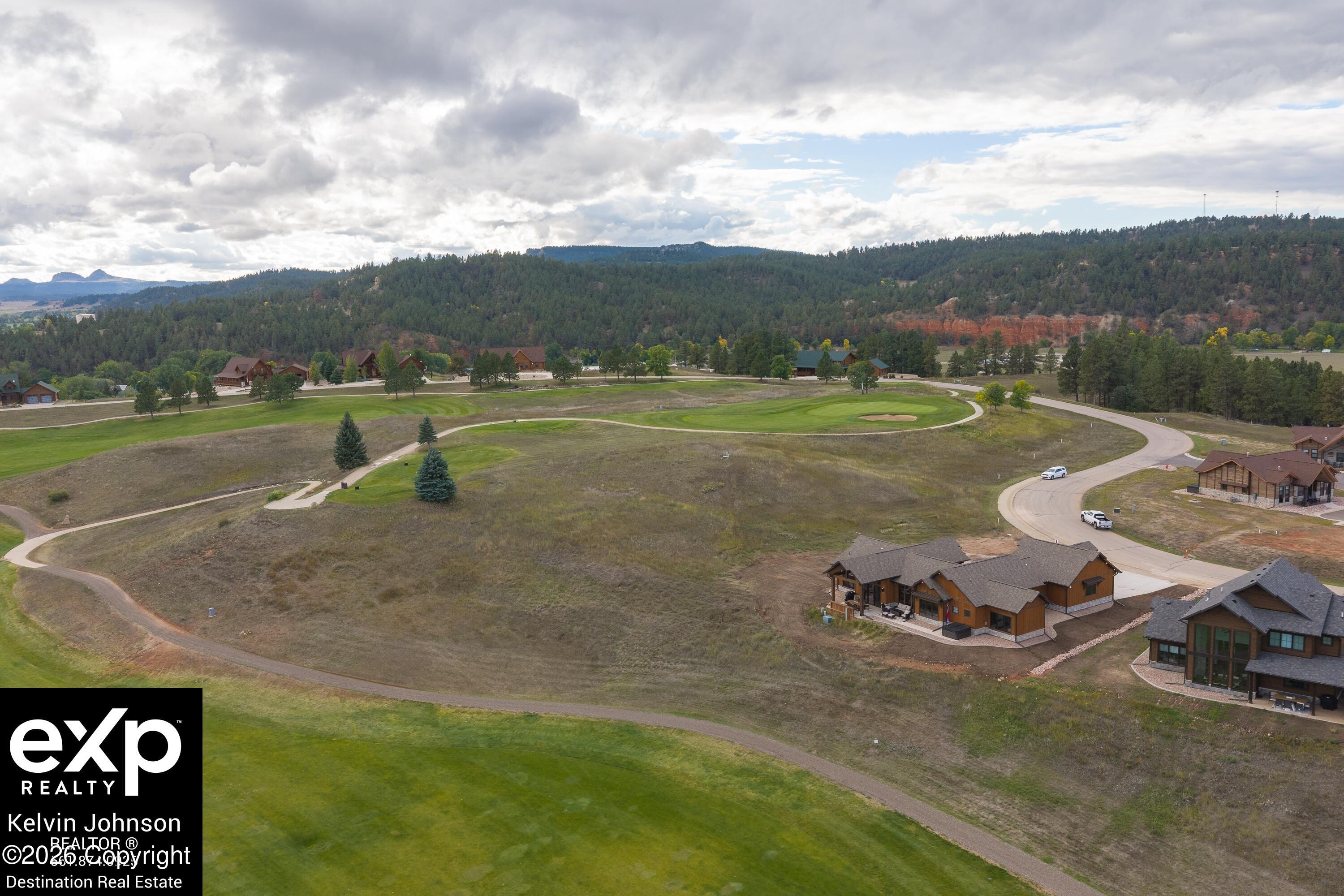 Aerial view of homes beside a golf course, with wooded hills and red rock formations in the distance.