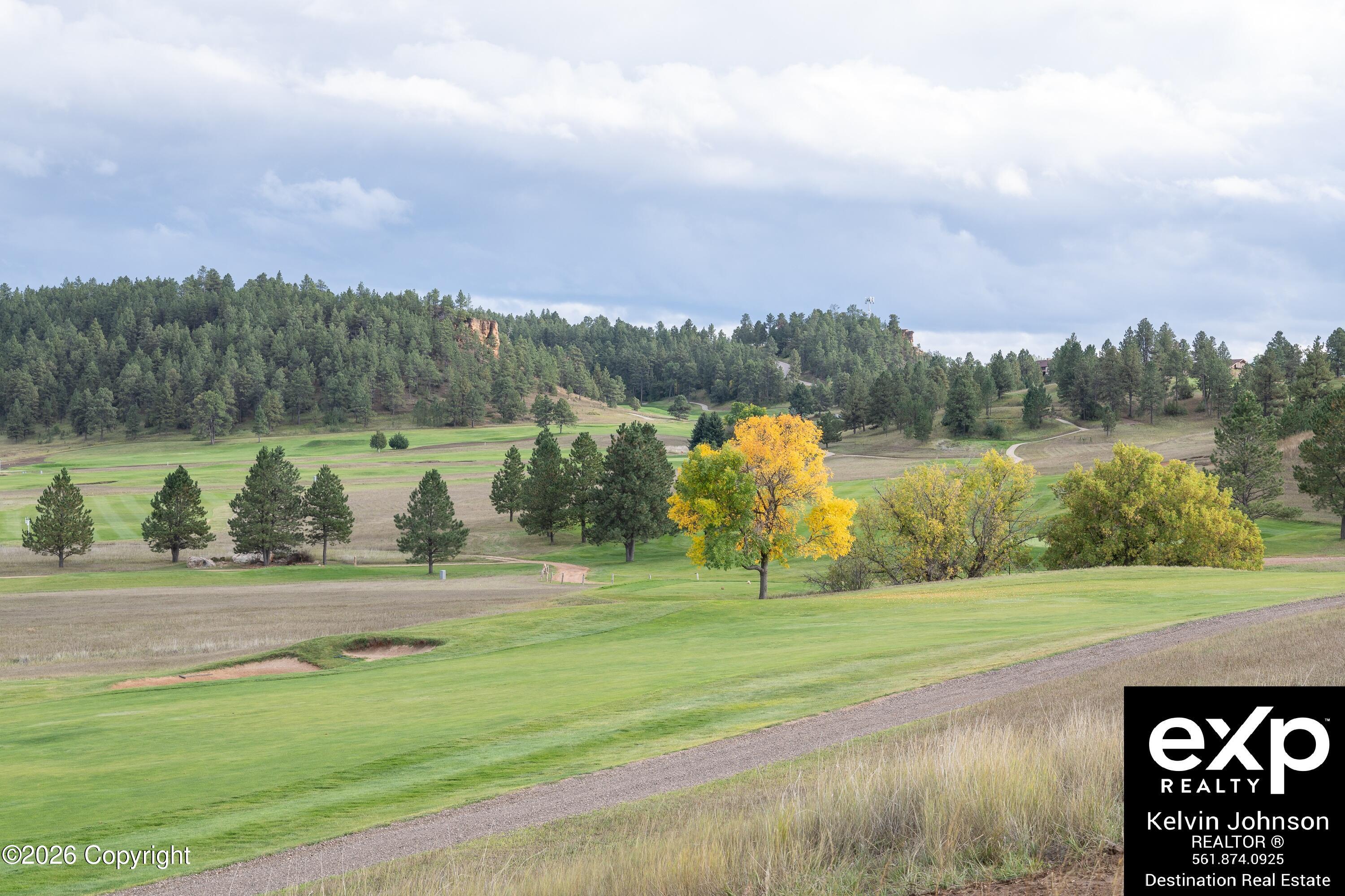 Golf course with rolling fairways, pine-covered hills, and bright yellow autumn trees.