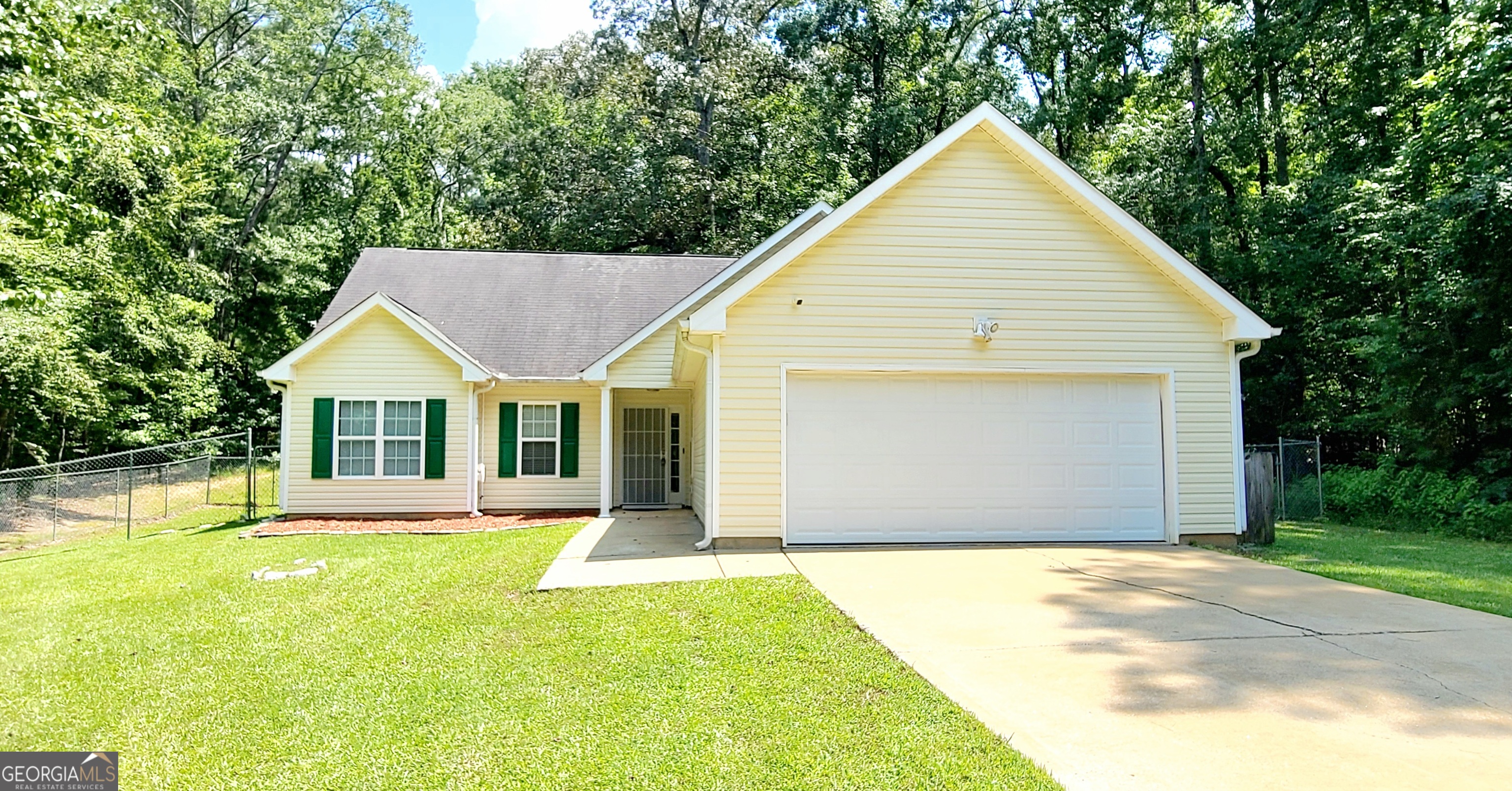 Cream-colored home with green shutters, a two-car garage, and a broad driveway amid mature trees.