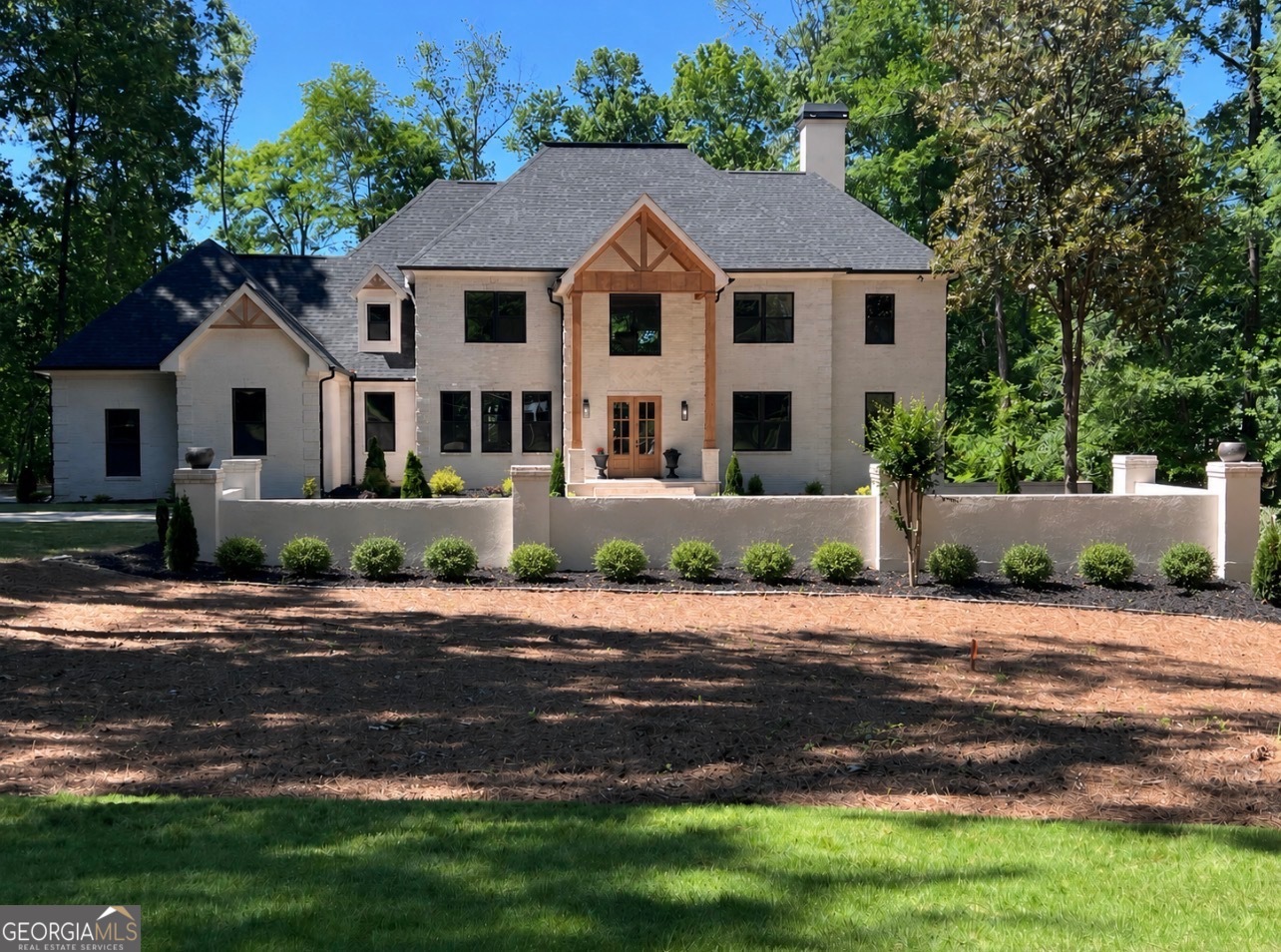 Light-brick home with a timber-trimmed entry, framed by trees behind a low garden wall.