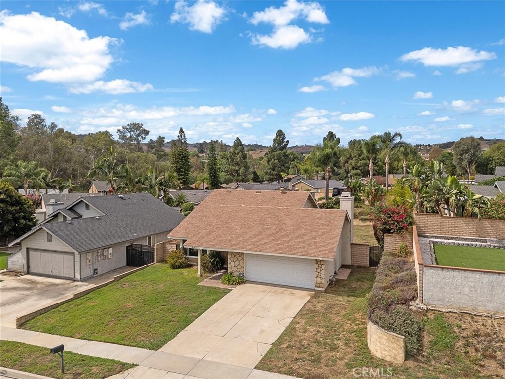 Single-story home with an attached garage and driveway, surrounded by neighboring homes and green hills.