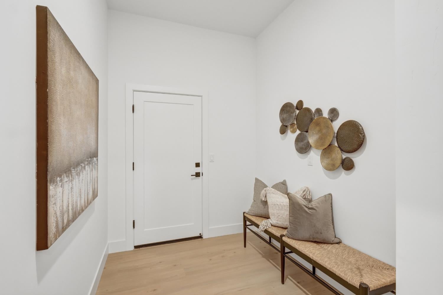 Entryway with a white front door, woven wall decor, and a long bench with neutral pillows.