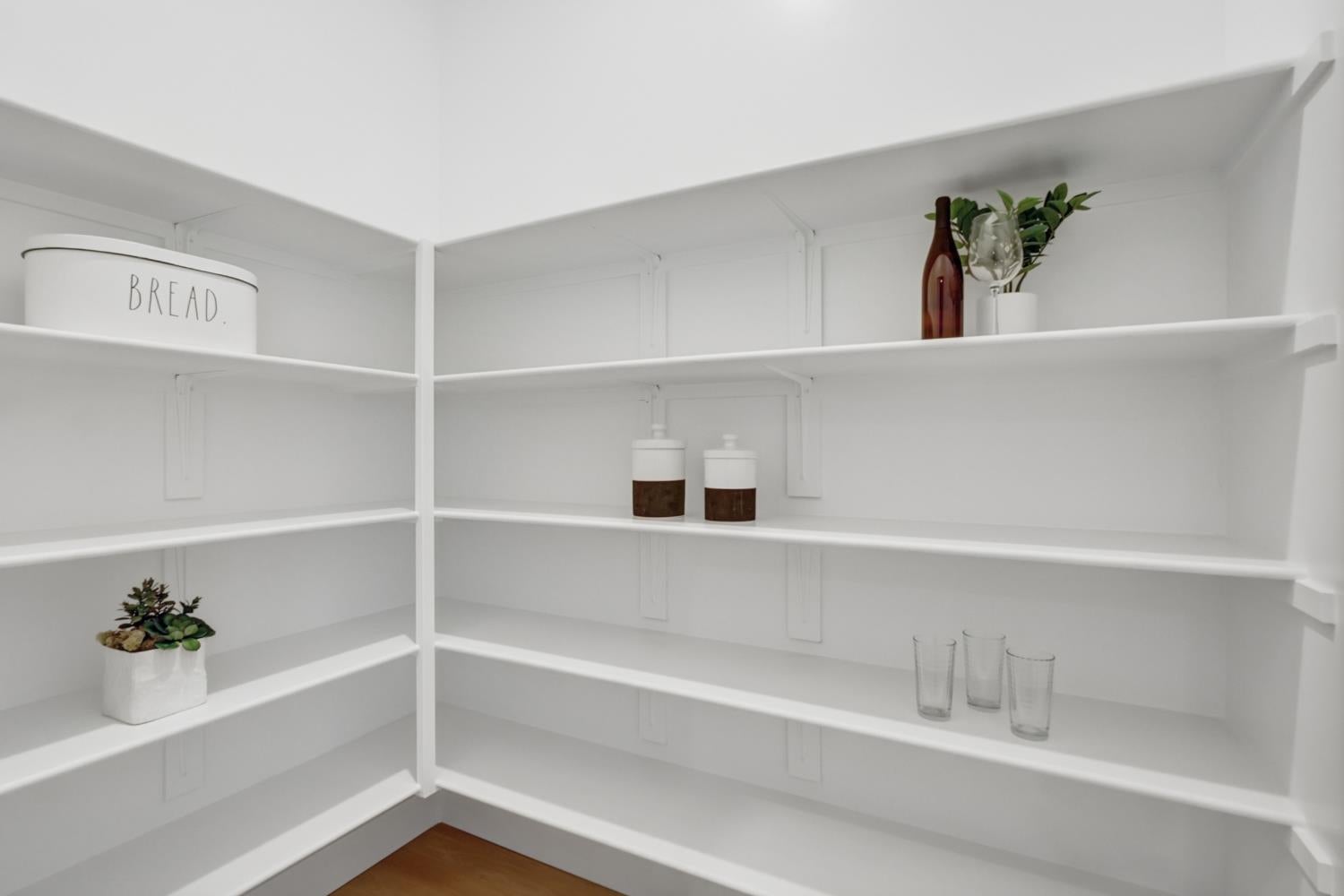 Walk-in pantry with white open shelves, a bread tin, glassware, jars, and small plants.