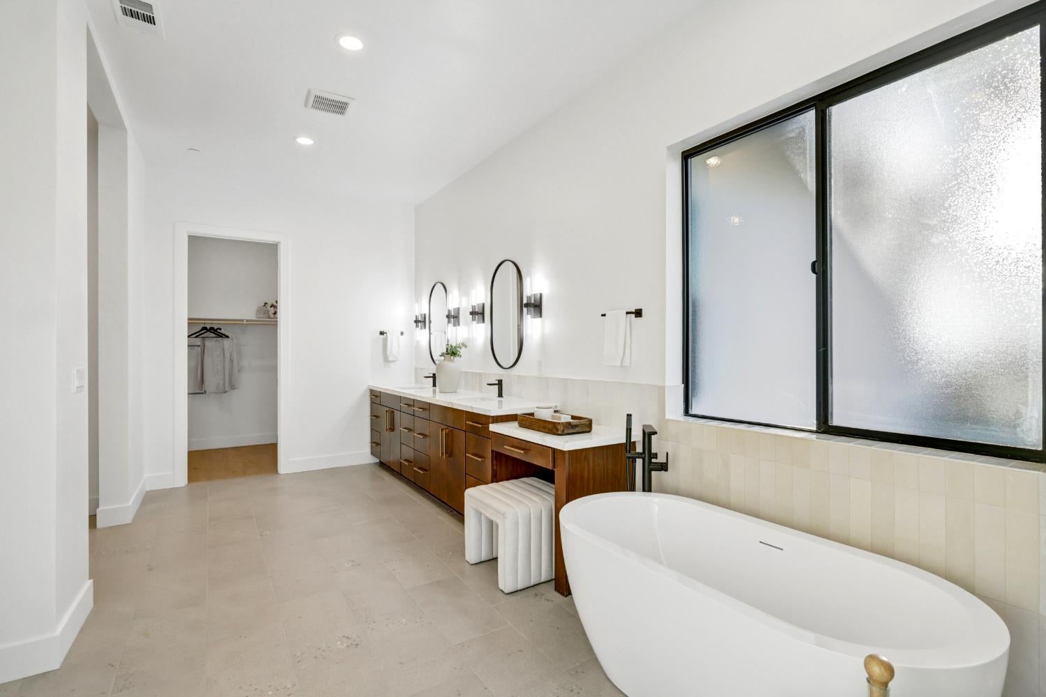 Primary bathroom with a freestanding soaking tub, frosted window, and dark wood double vanity.
