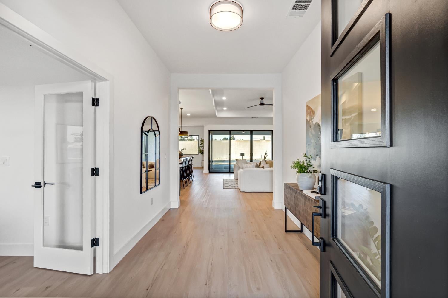 Bright entryway with light wood floors, glass-paneled front door, and view toward living area and pool.
