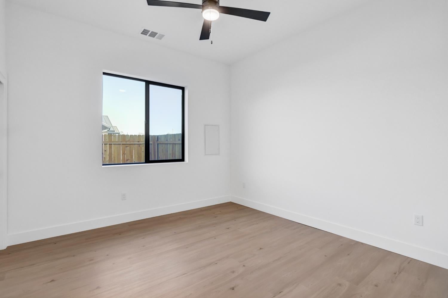 Vacant bedroom with light wood floors, a black-framed window, and a ceiling fan.