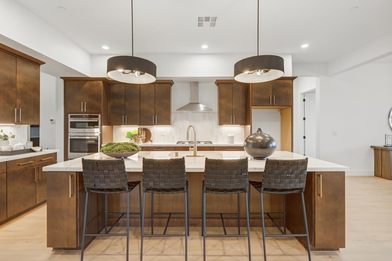 Modern kitchen with dark wood cabinets, double oven, and a large island with four bar stools.