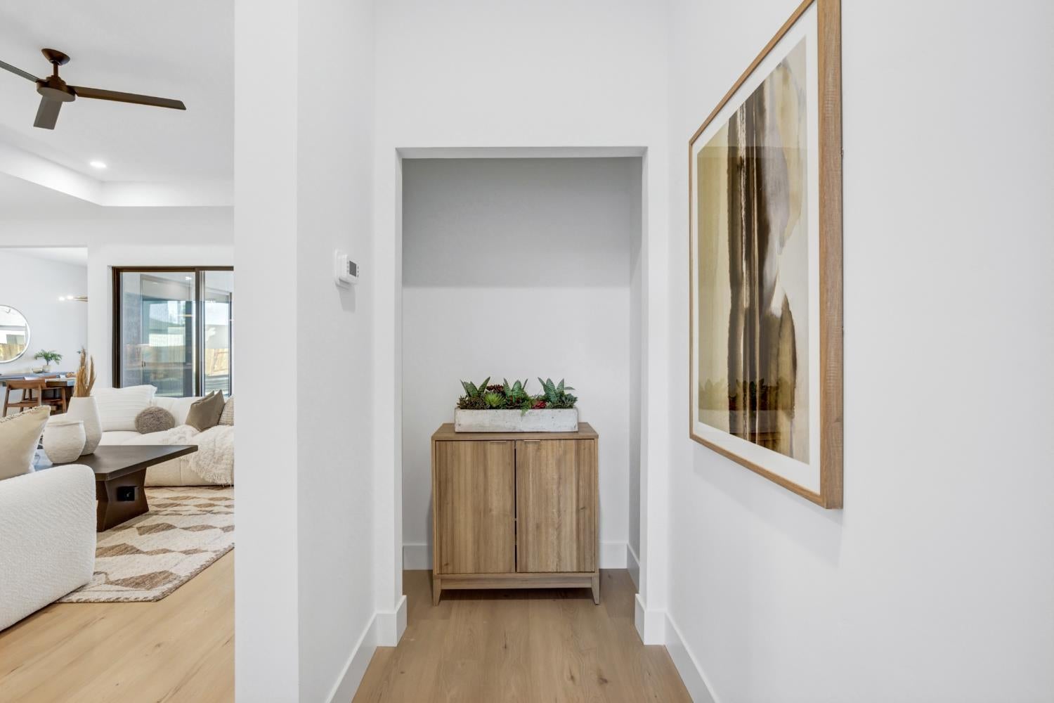 Entry hall with a wooden console and planter, framed abstract art, and the living area beyond.