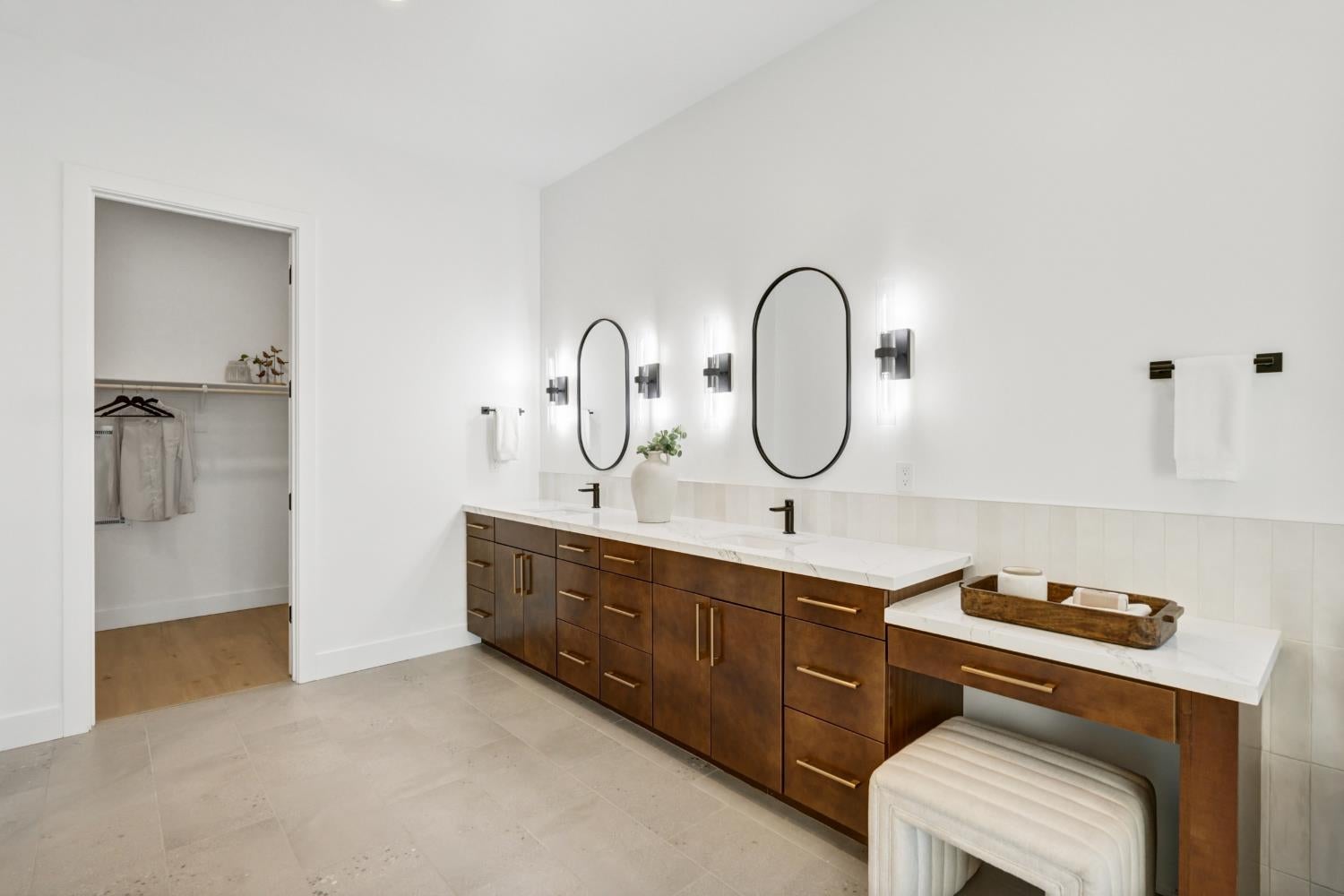 Bathroom with a double-sink wood vanity, oval mirrors, and an open closet doorway.