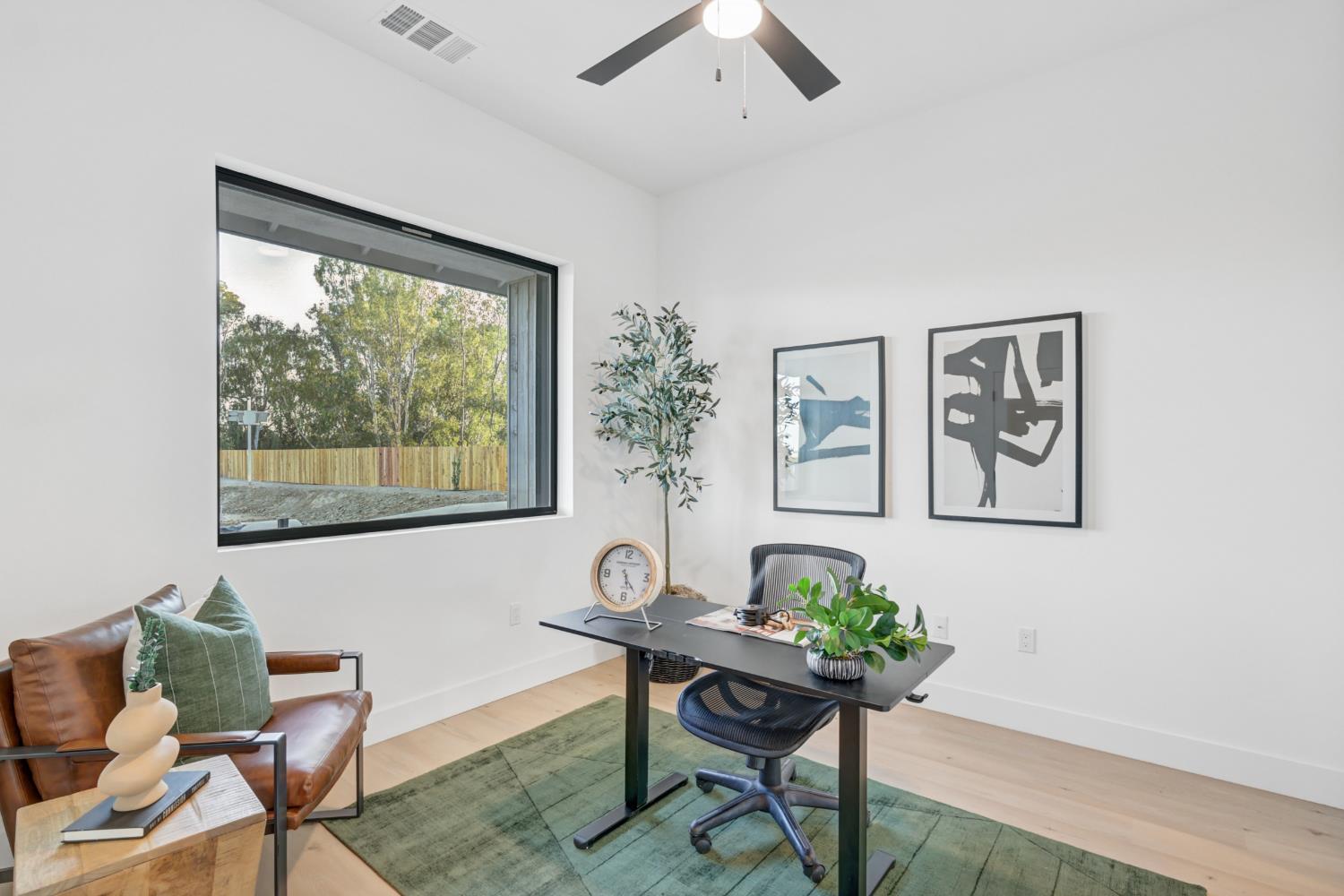Furnished home office with a black desk, leather armchair, and large window overlooking trees.
