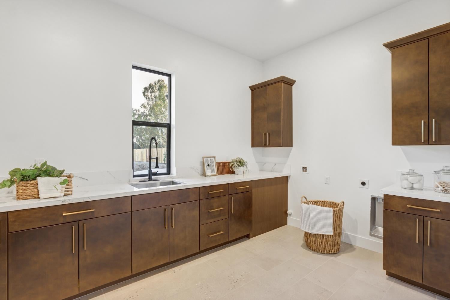 Laundry room with dark wood cabinets, white countertops, and a utility sink beneath a tall window.