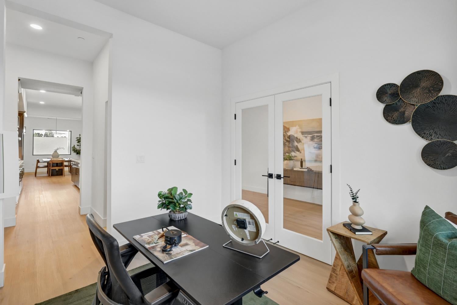 Furnished home office with a black desk, glass-paneled doors, and a view toward the dining area.