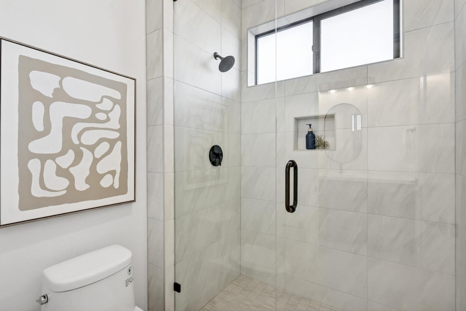 Bathroom with a tiled glass walk-in shower, black fixtures, and a high window.