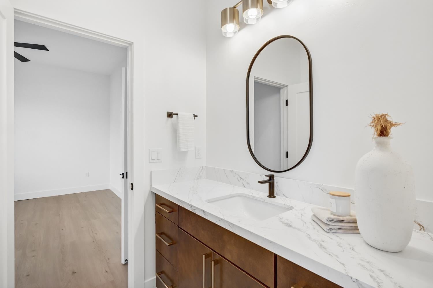 Modern bathroom vanity with a marble-look counter, dark wood drawers, bronze faucet, and oval mirror.