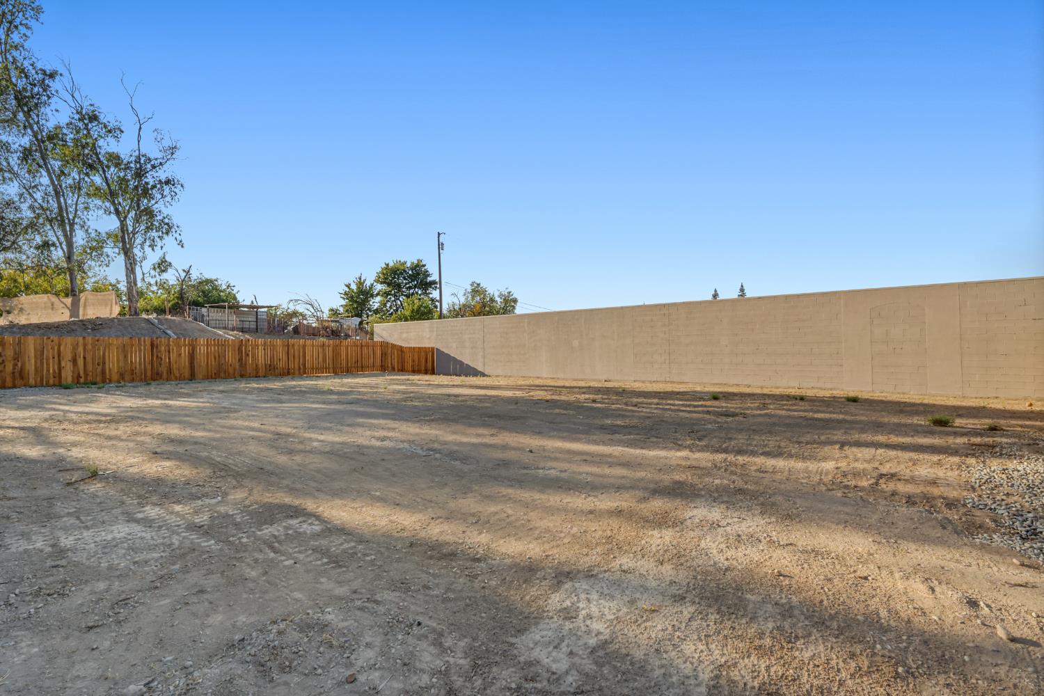 Bare dirt lot enclosed by a wooden fence and a tall block wall.