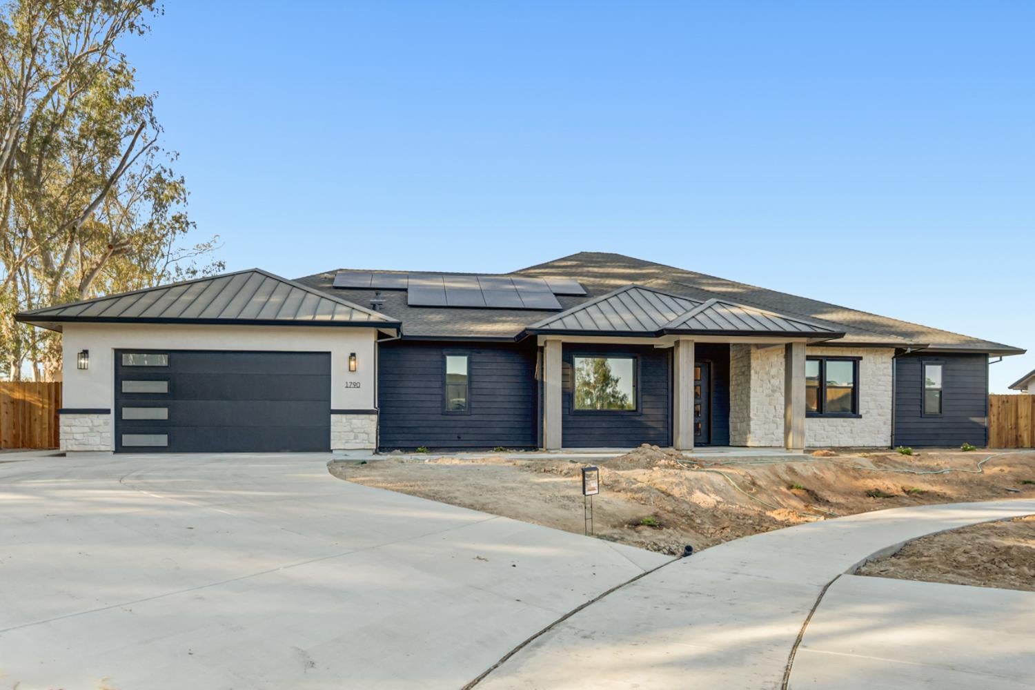 Single-story dark blue home with stone accents, rooftop solar panels, and a wide concrete driveway.