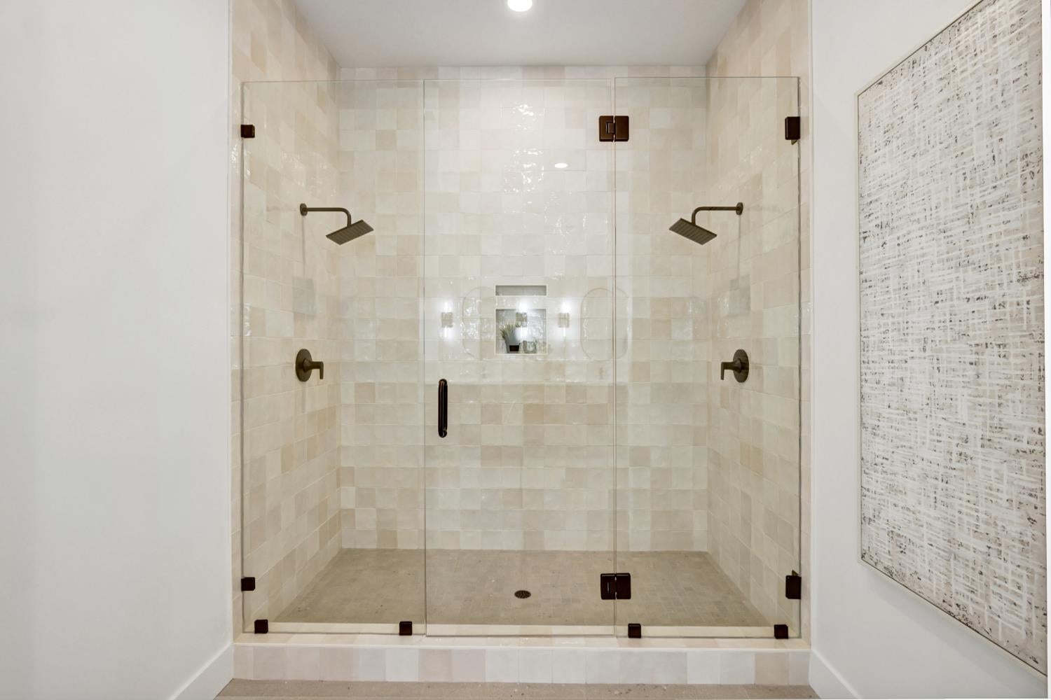 Walk-in shower with frameless glass, cream tile, dual rainfall showerheads, and a recessed wall niche.