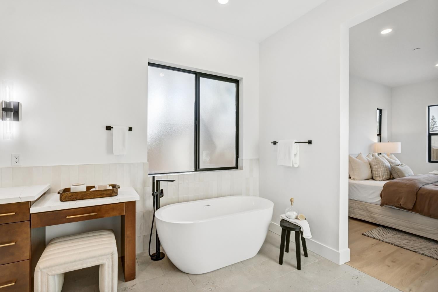 Modern bathroom with a freestanding soaking tub, dark wood vanity, and adjoining bedroom.