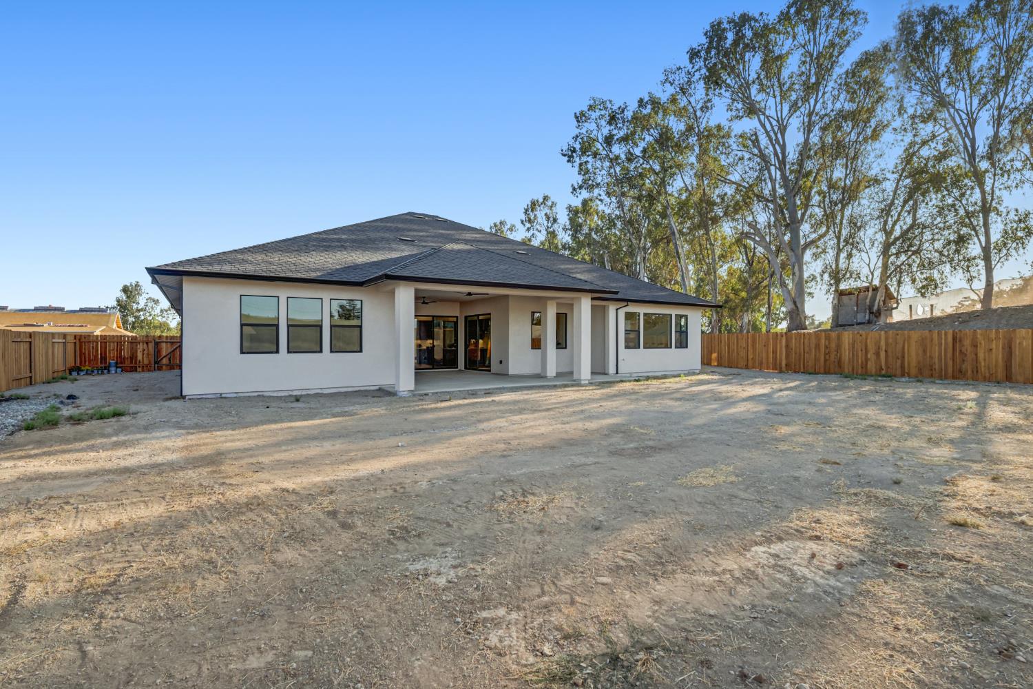 Rear of a single-story white house with a covered patio and a large bare, fenced backyard.