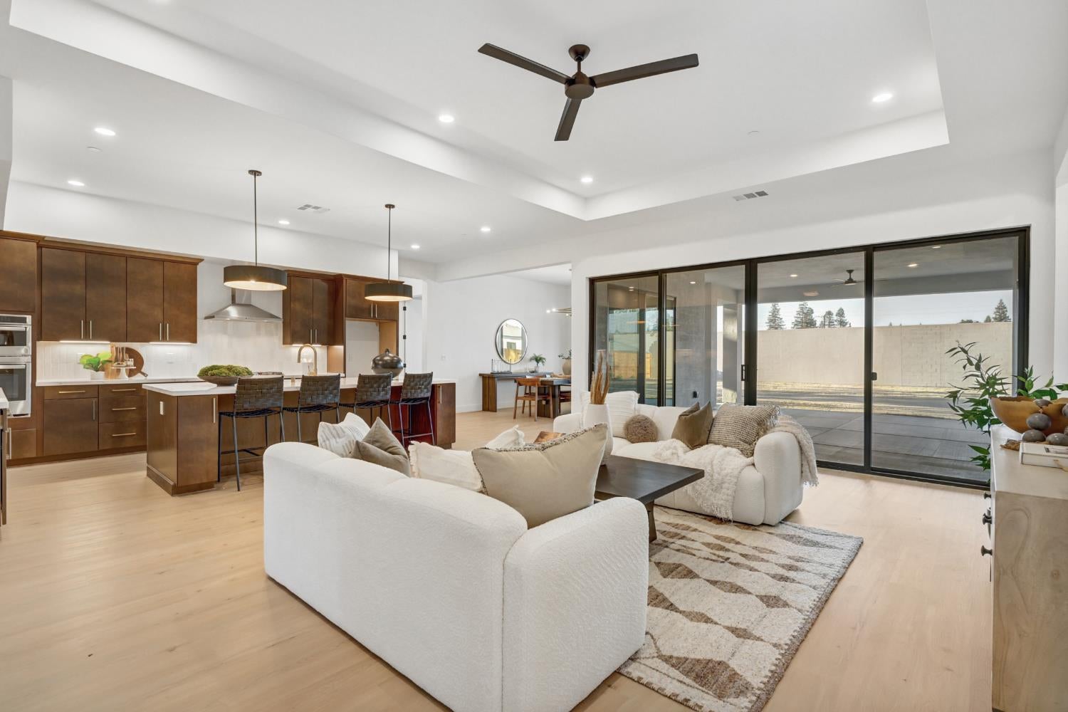Open-plan living room and kitchen with dark cabinetry, white seating, and sliding doors to a covered patio.