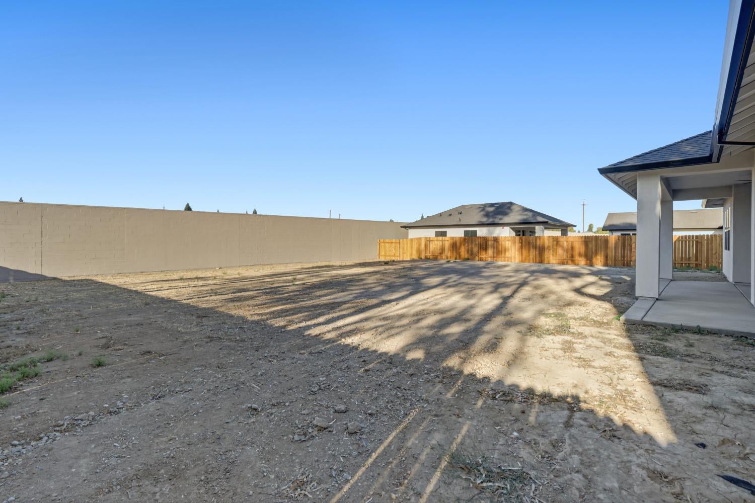 Bare dirt backyard enclosed by masonry and wooden fencing, with a covered patio.