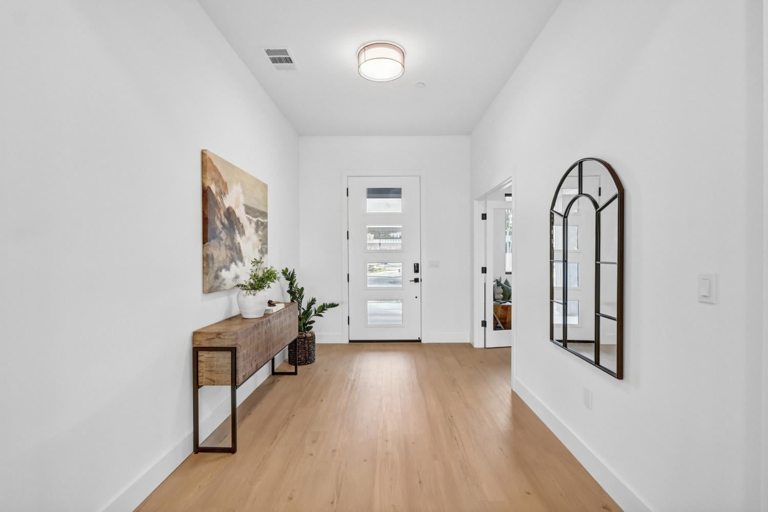 Bright entryway with a glass-paneled front door, wood console table, plants, and arched mirror.