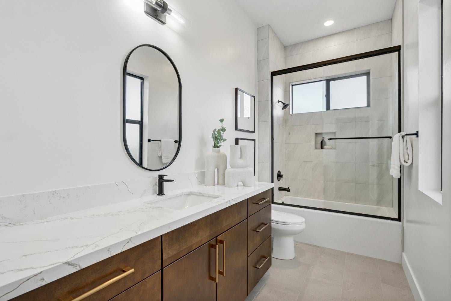 Bathroom with a veined stone vanity, dark wood cabinetry, and a black-framed glass tub-shower enclosure.