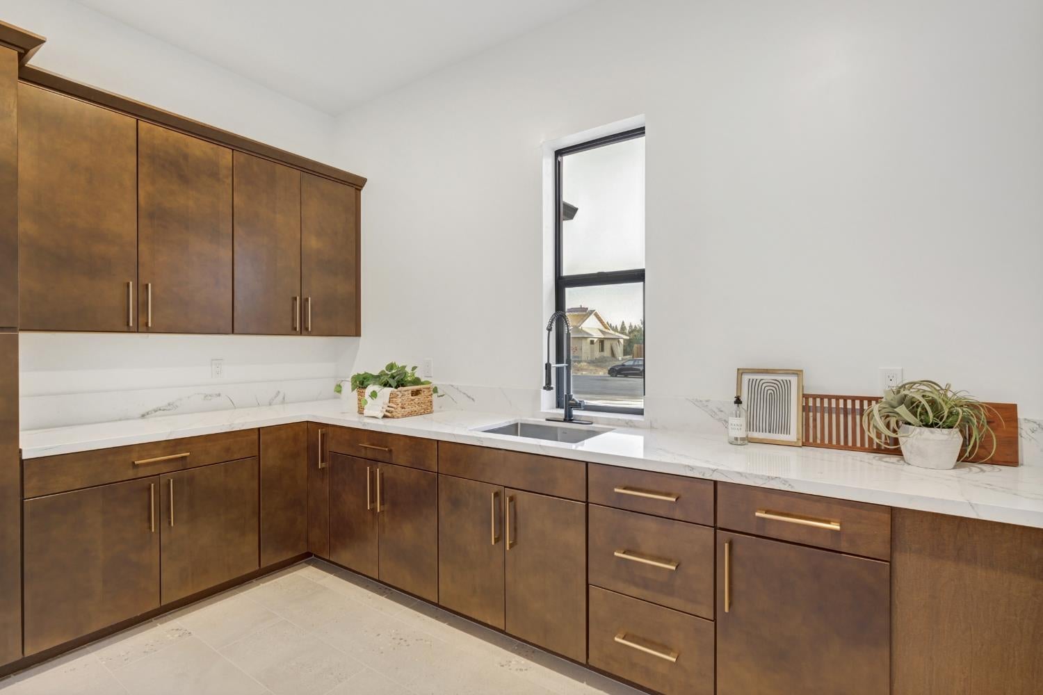 Kitchen with dark brown cabinets, brass hardware, and a white countertop around a window-side sink.