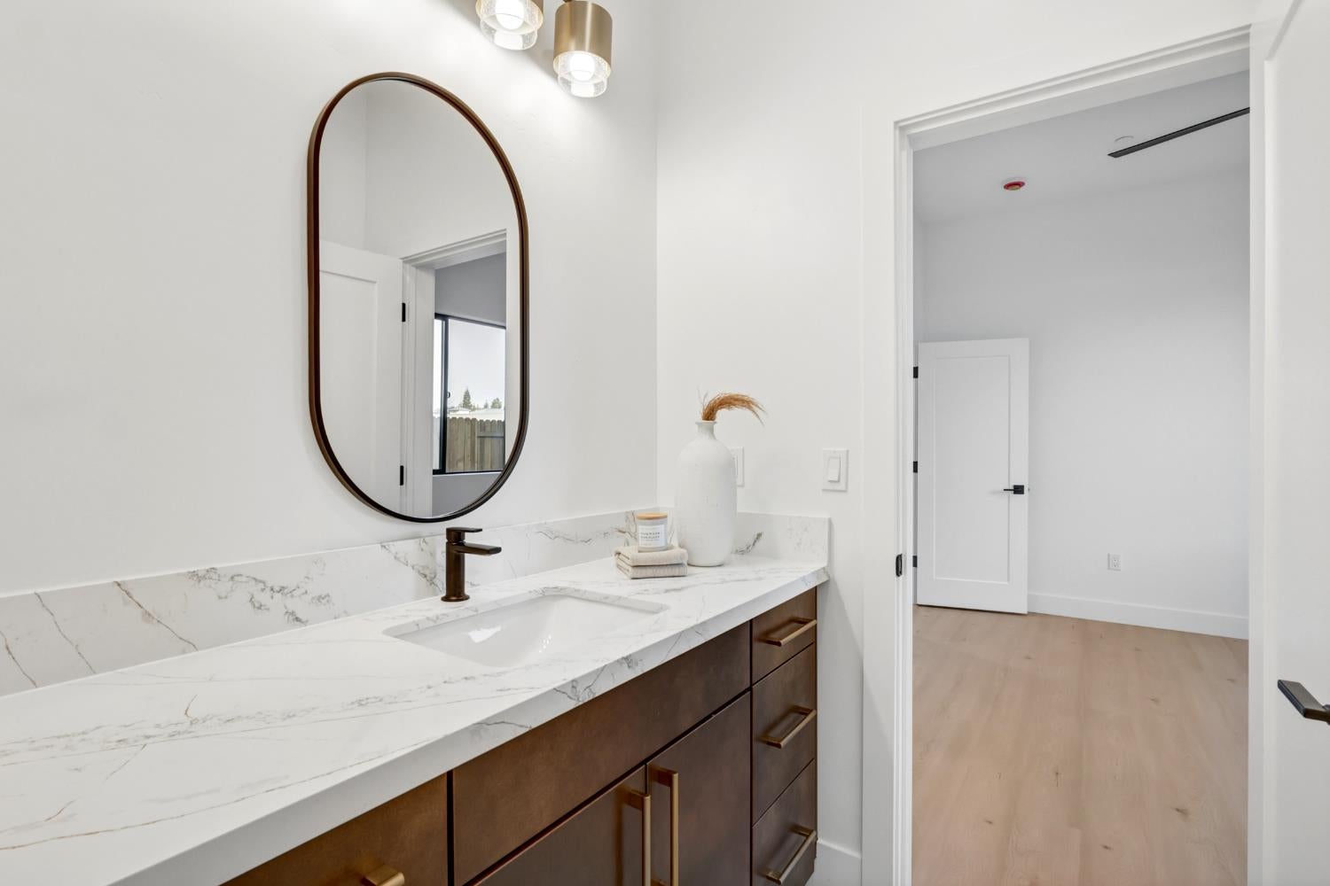 Bathroom vanity with veined white countertop, dark wood cabinets, bronze faucet, and oval mirror.
