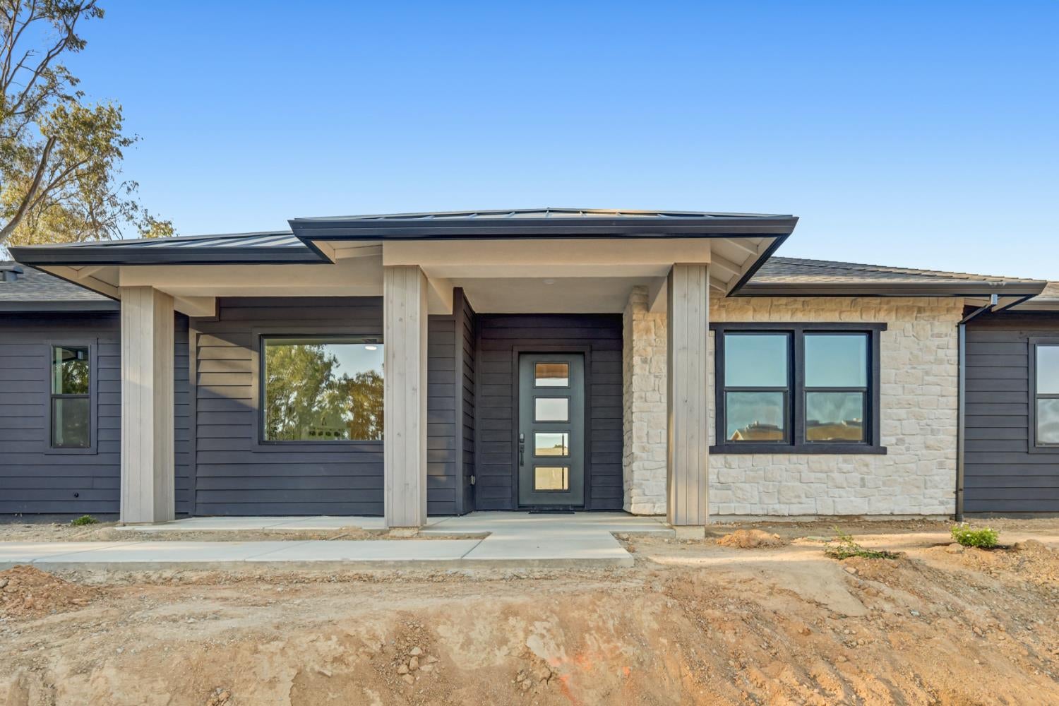 Modern home entrance with dark siding, light stone facade, and a broad covered porch.