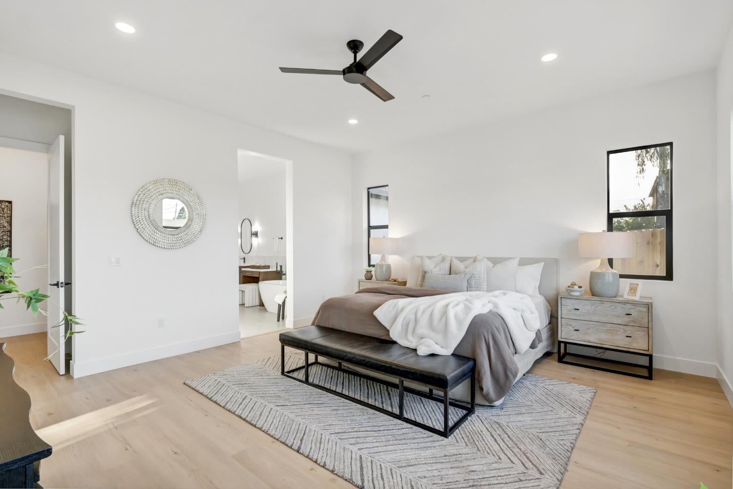 Staged bedroom with a low platform bed, ceiling fan, and doorway to an ensuite bathroom.