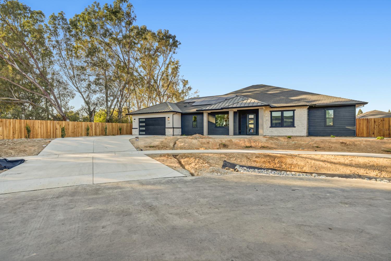 Modern single-story home with rooftop solar panels, a two-car garage, and an unfinished front yard.