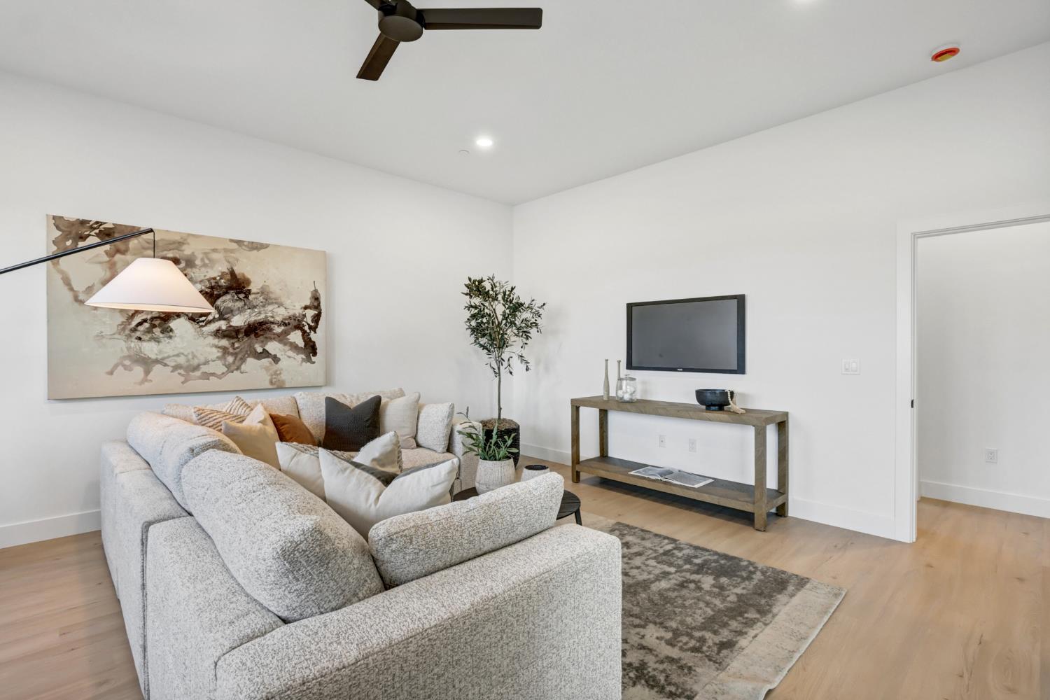 Staged living room with a light-gray sectional, abstract wall art, and a television console.
