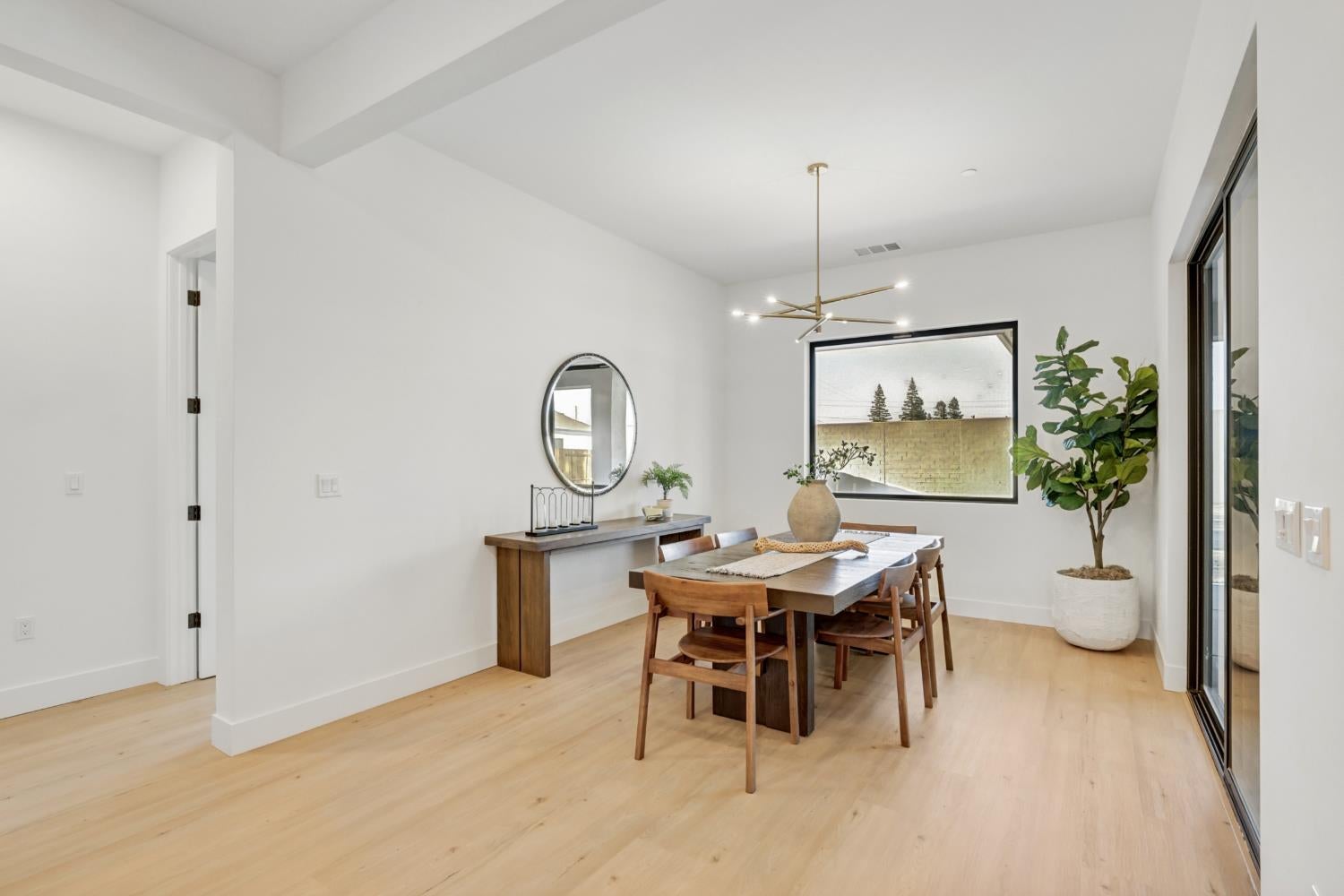 Staged dining room with a wooden table, brass chandelier, light wood floors, and large windows.