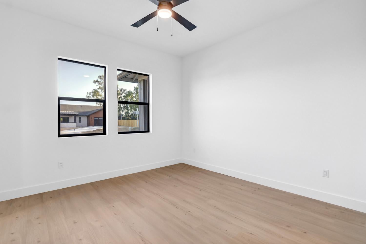 Vacant room with light wood flooring, two black-framed windows, and a ceiling fan.