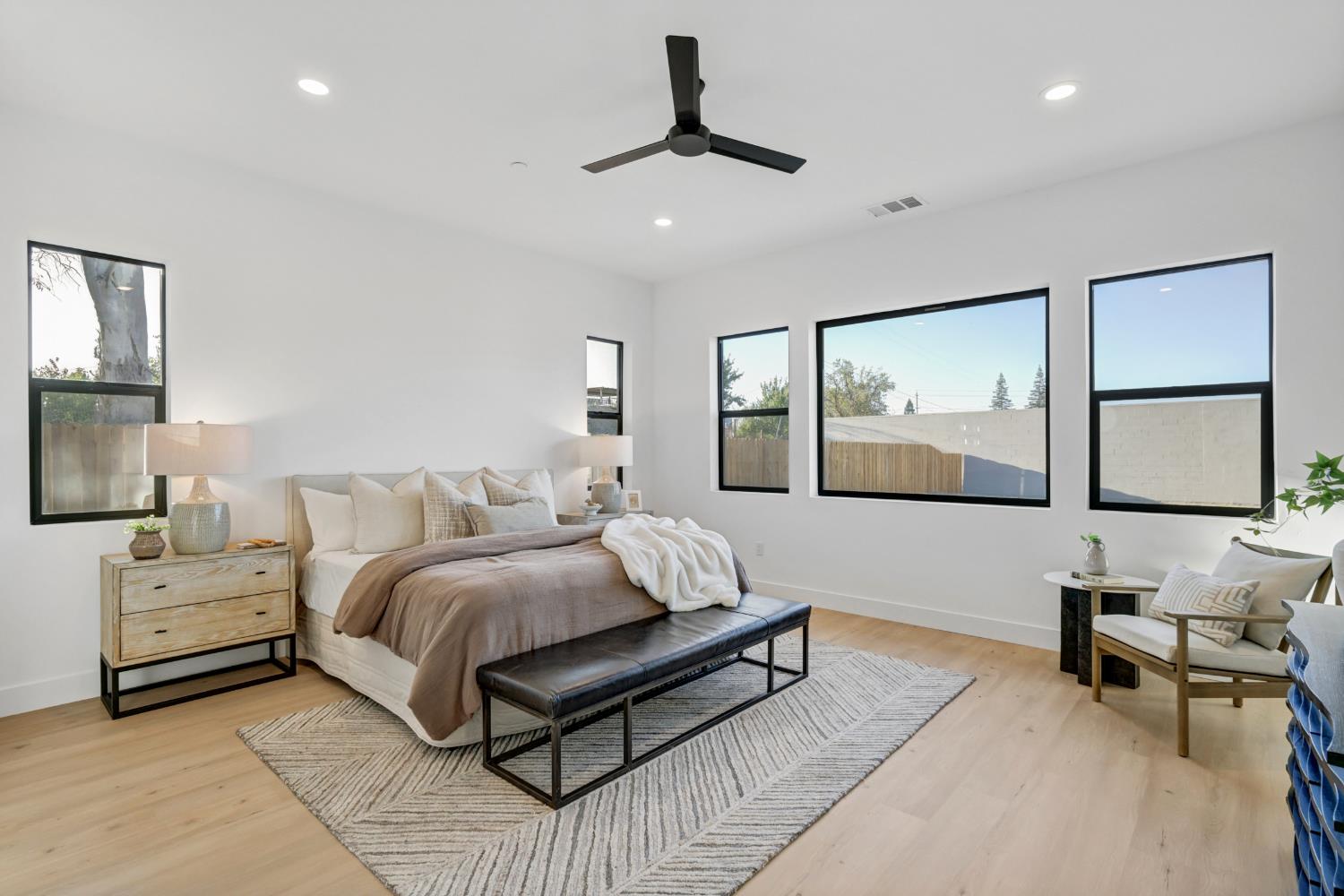 Staged bedroom with a large bed, dark bench, patterned rug, and black-framed windows.