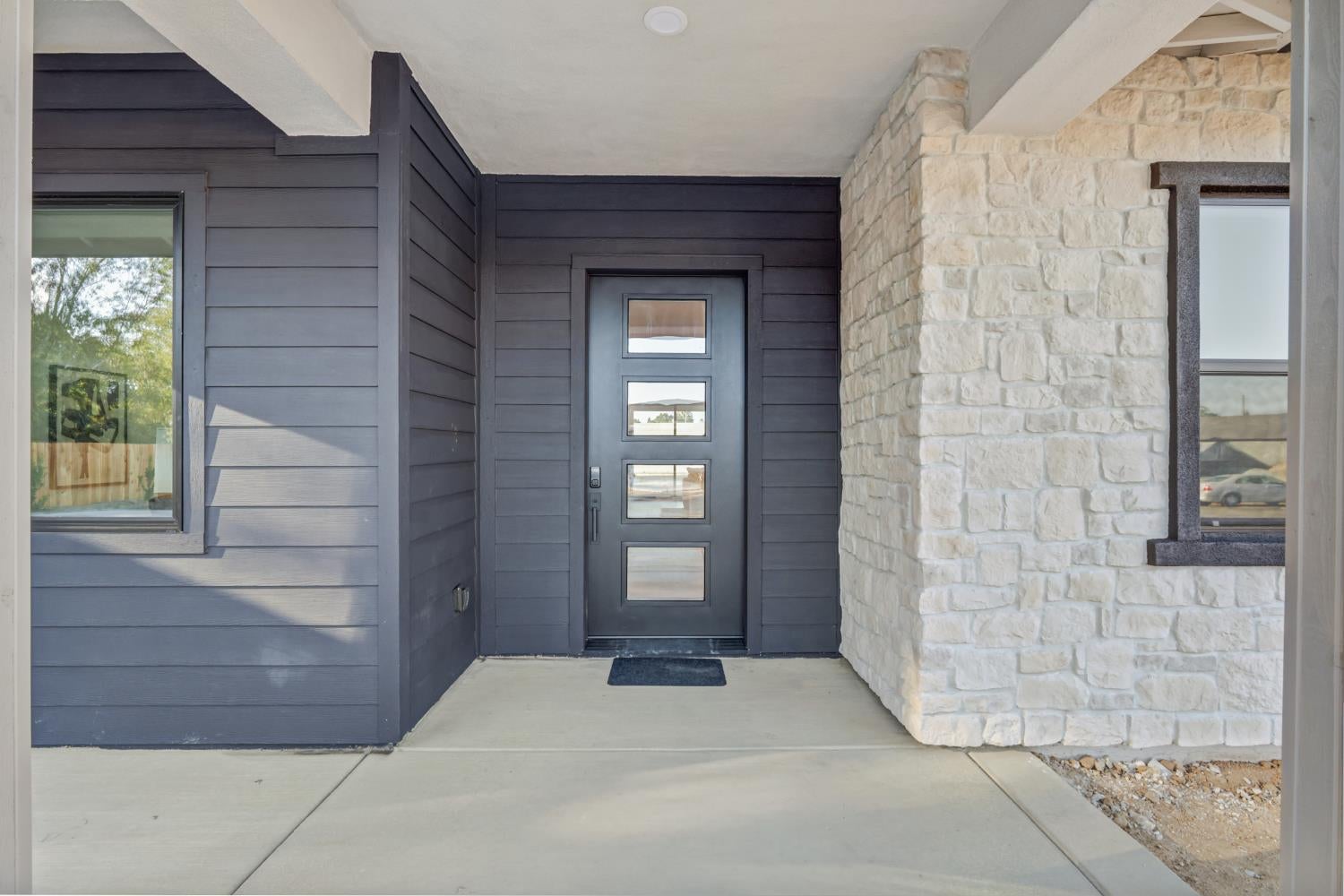 Covered home entry with a glass-panel door, dark siding, and a light stone accent wall.