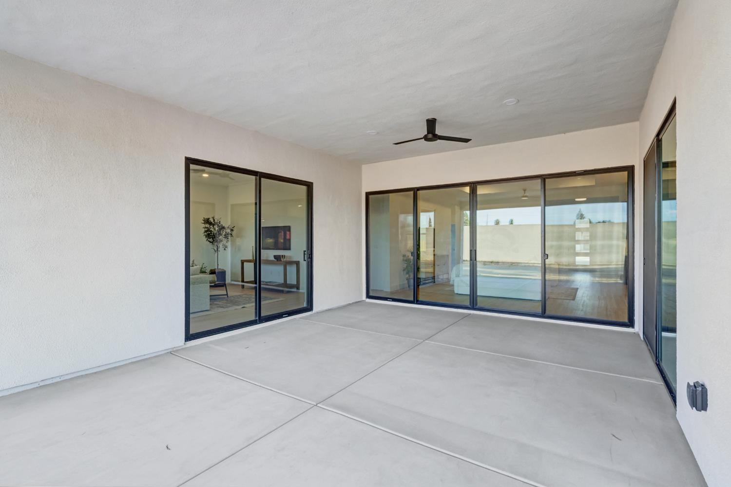 Covered patio with concrete flooring, ceiling fan, and wide sliding glass doors.