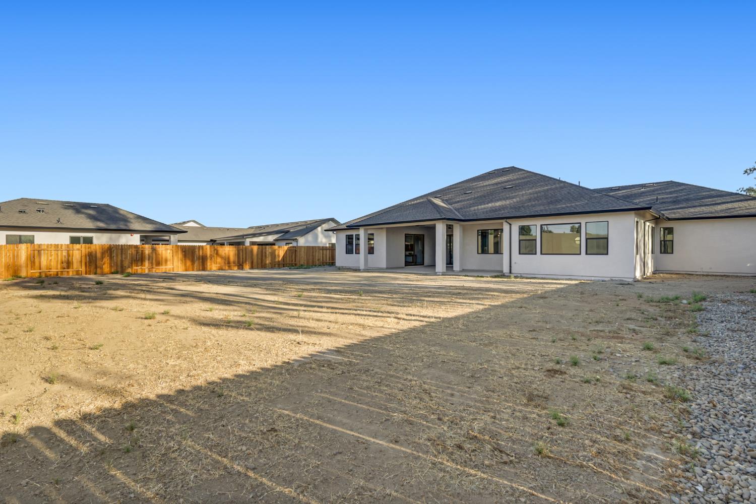 Rear exterior of a single-story white home with a fenced, unfinished dirt yard.