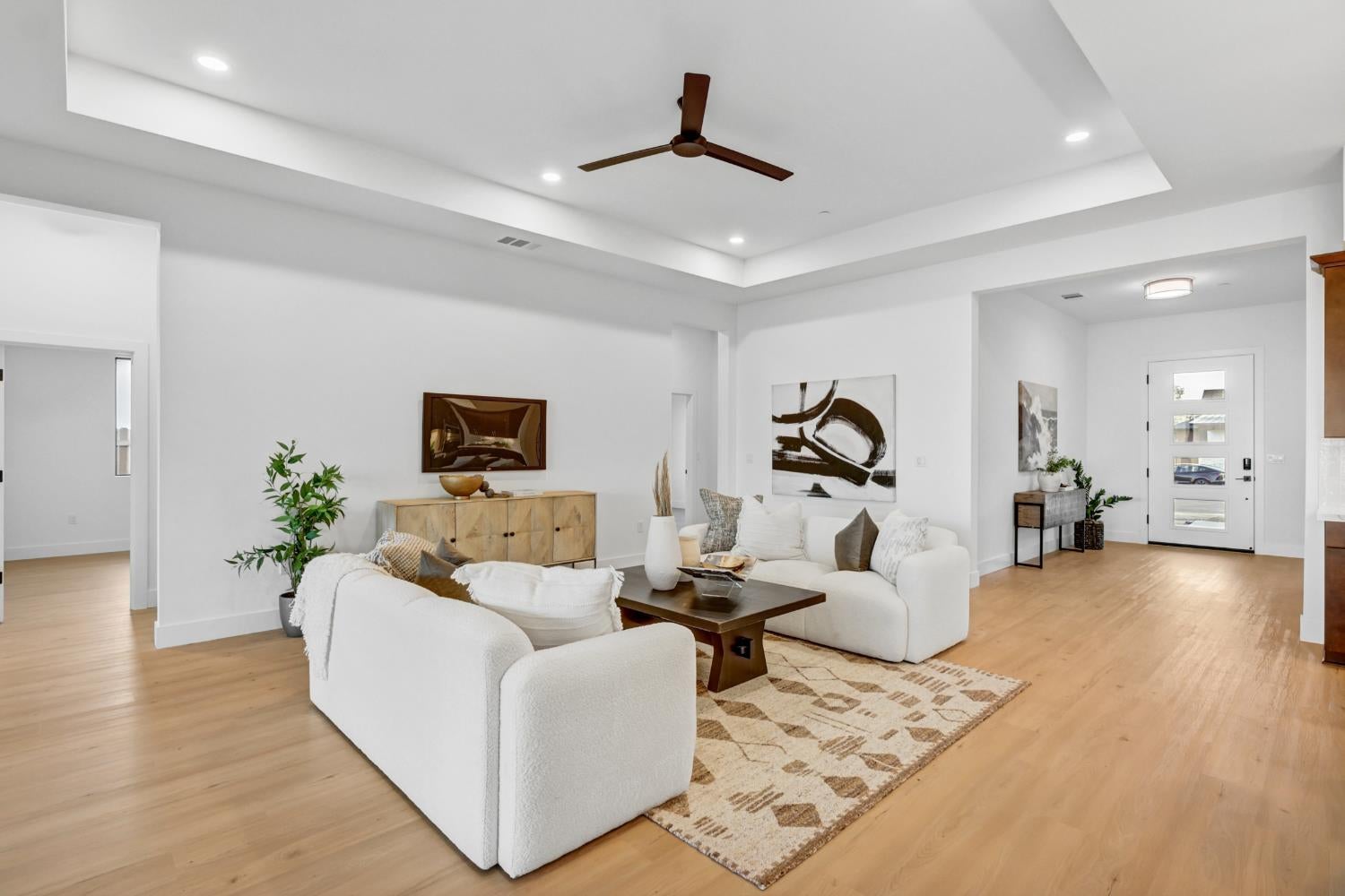 Staged living room with white sofas, a patterned rug, light wood floors, and a tray ceiling.