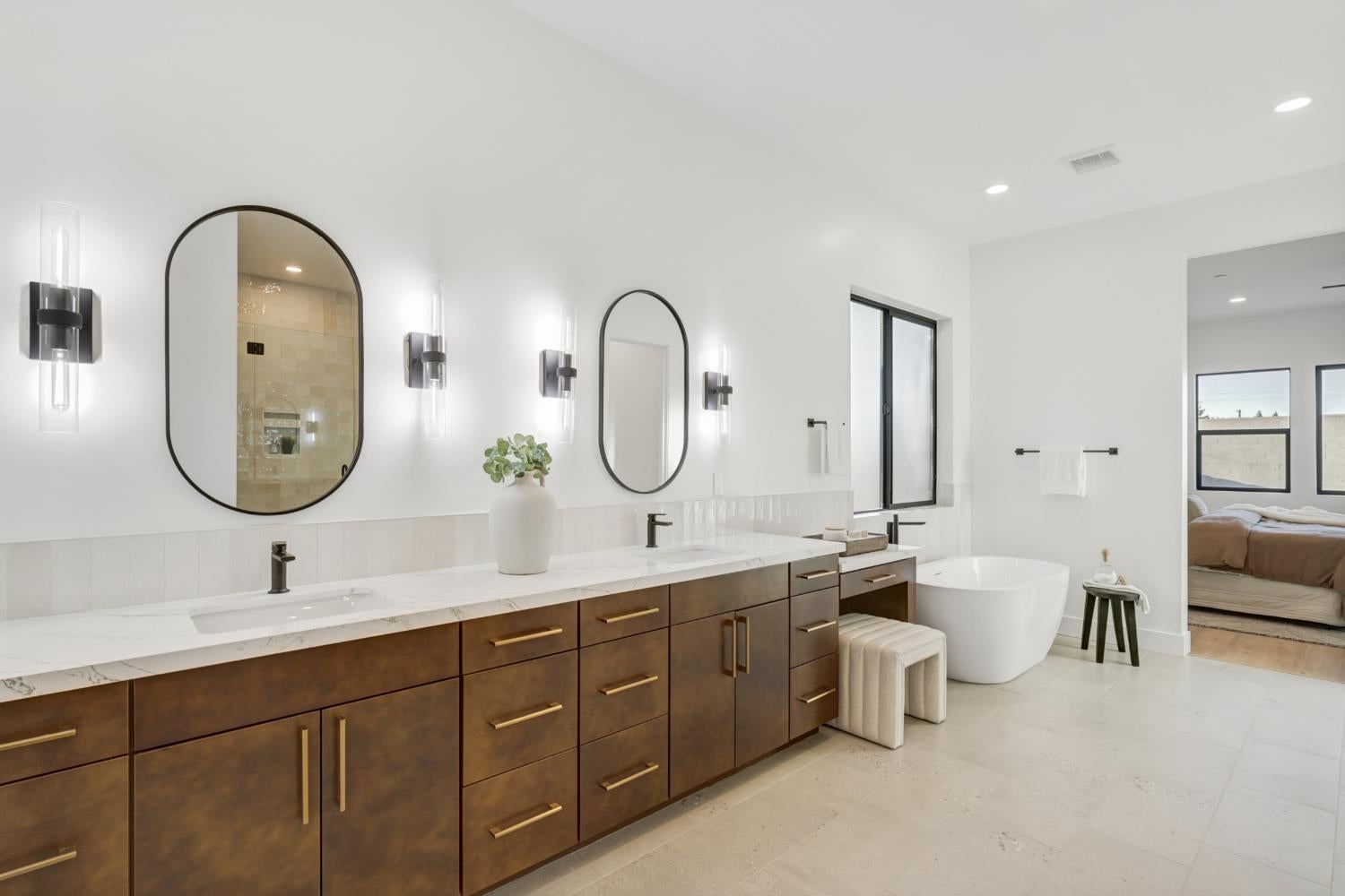 Modern bathroom with a long double vanity, arched mirrors, and a freestanding soaking tub.